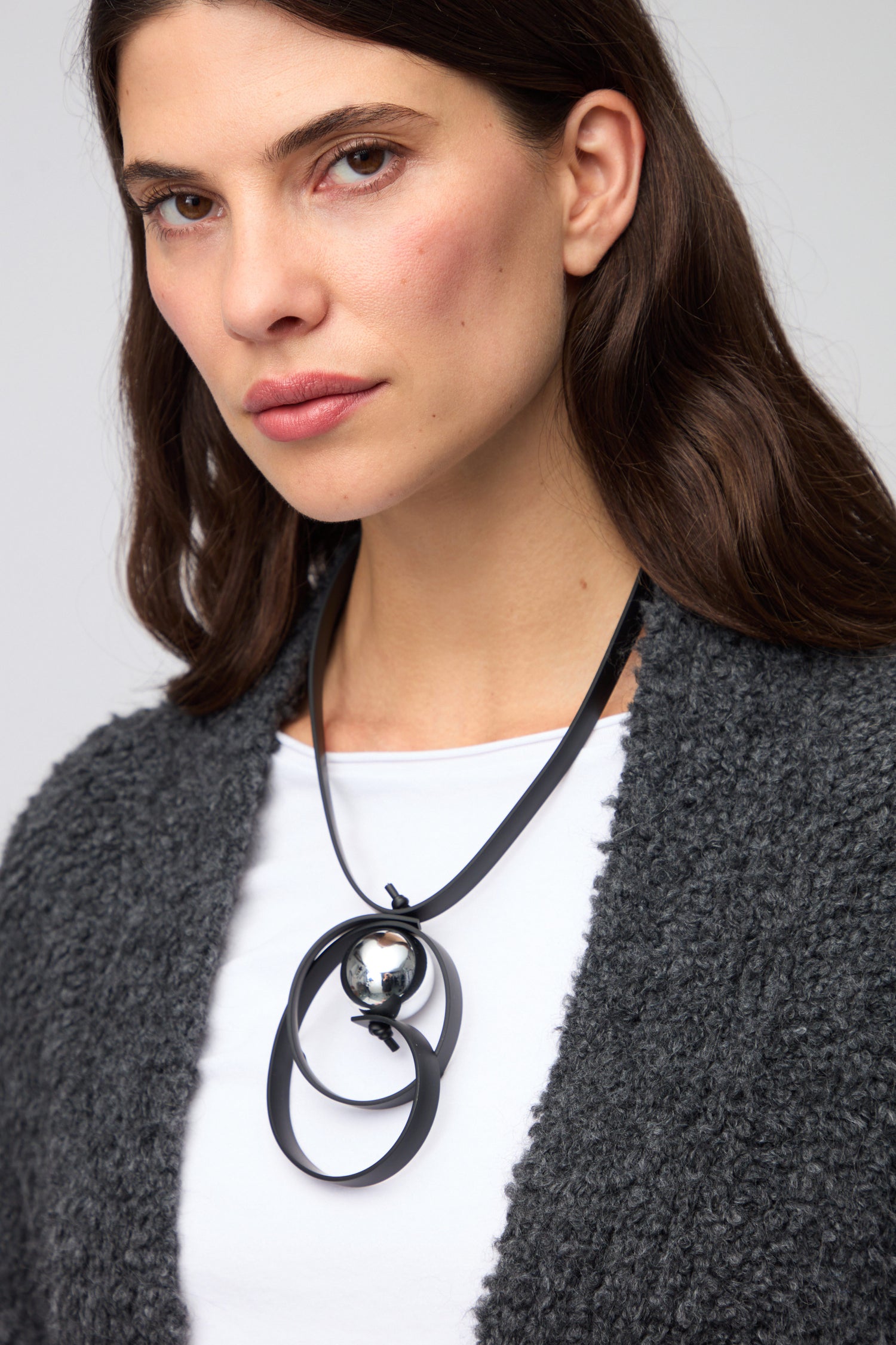 Woman wearing a grey textured cardigan, white shirt, and the Penseur Silver Sphere Necklace featuring circular pendants and a striking metallic silver sphere.