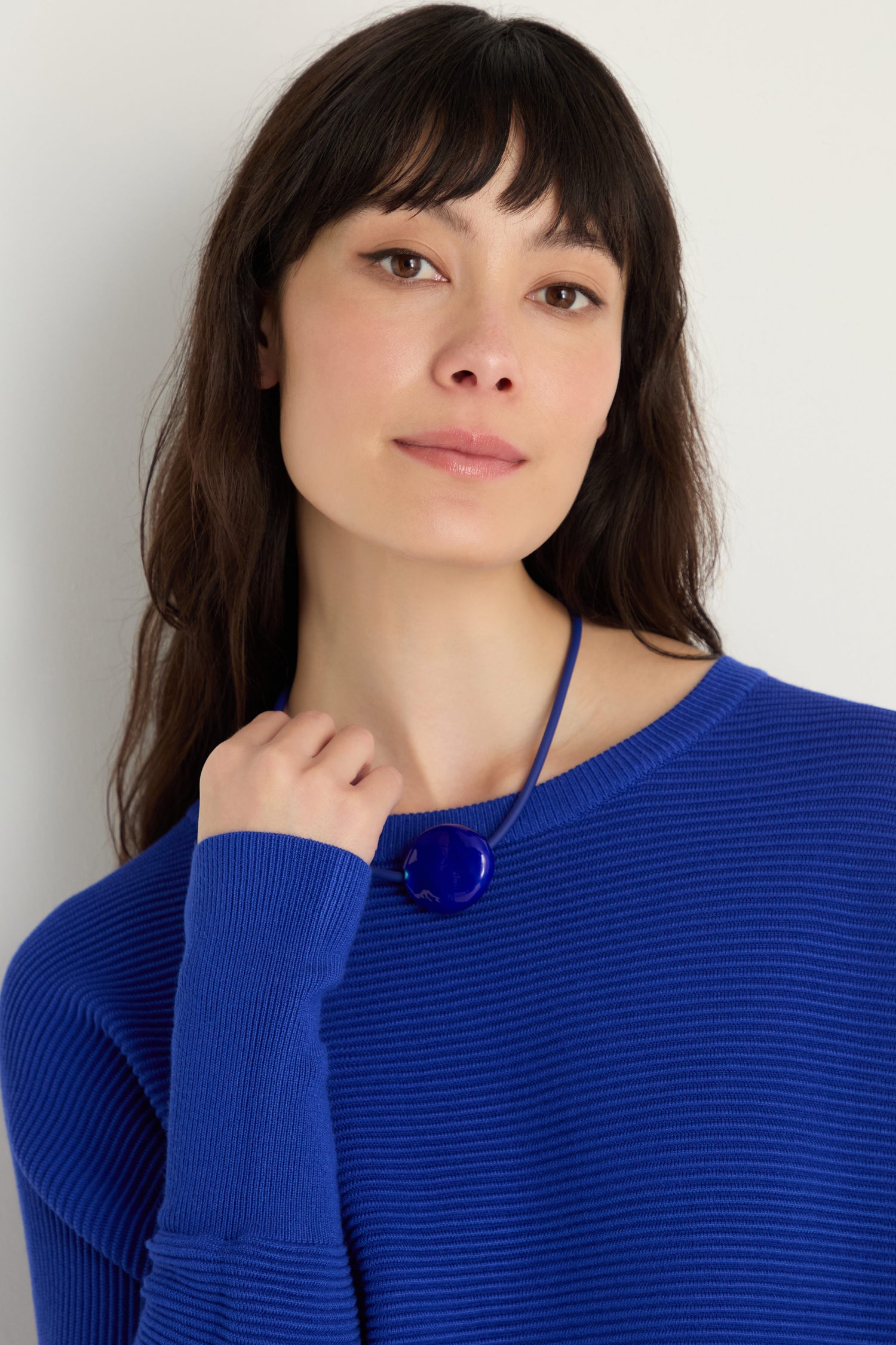 Woman with long dark hair wears a blue ribbed sweater and the Murano Glass Pebble Necklace, standing against a plain white background.