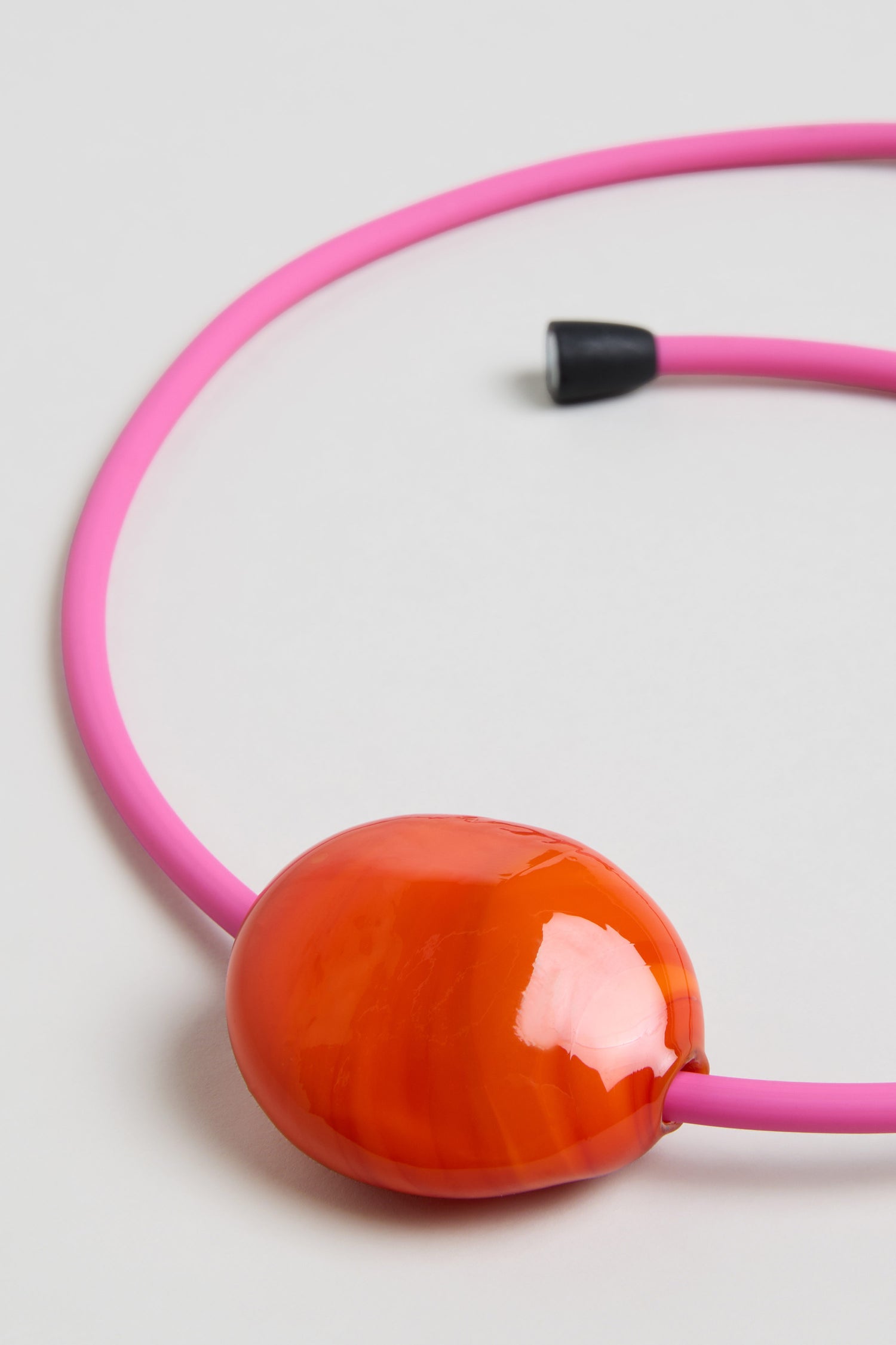 The Murano Glass Pebble Necklace features pink pebbles, a large glossy orange statement bead, and a black clasp, all displayed on a white background.