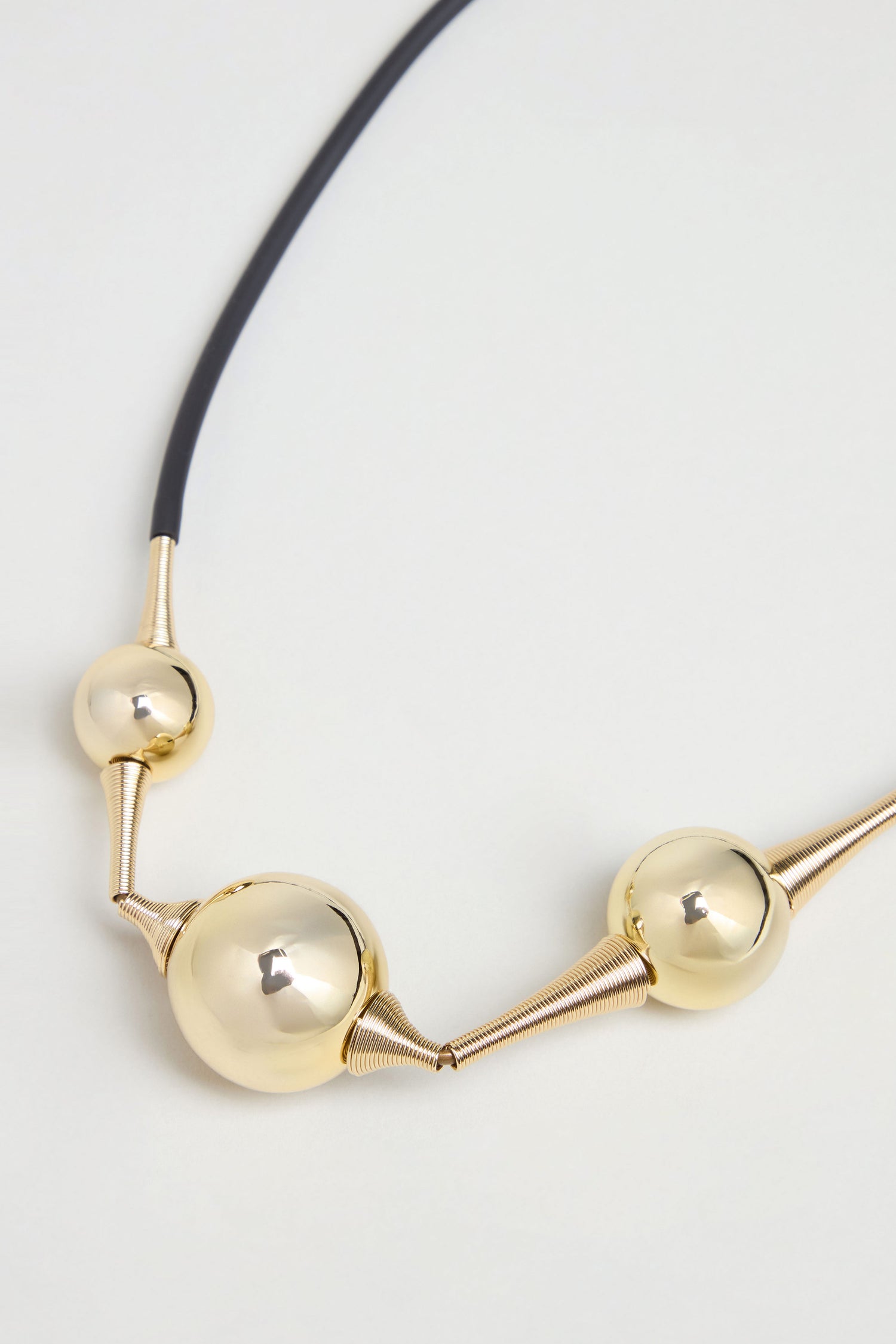 Cosmos Necklace featuring three large, shiny spherical beads connected by coiled metal sections on a black cord, capturing the essence of sculptural jewelry and modern design. Shown against a light background.