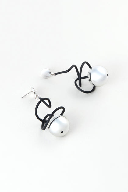 The Graphic Squiggle Earrings by Samuel Coraux showcase large white pearls and black abstract wire loops, presented on a plain white background.