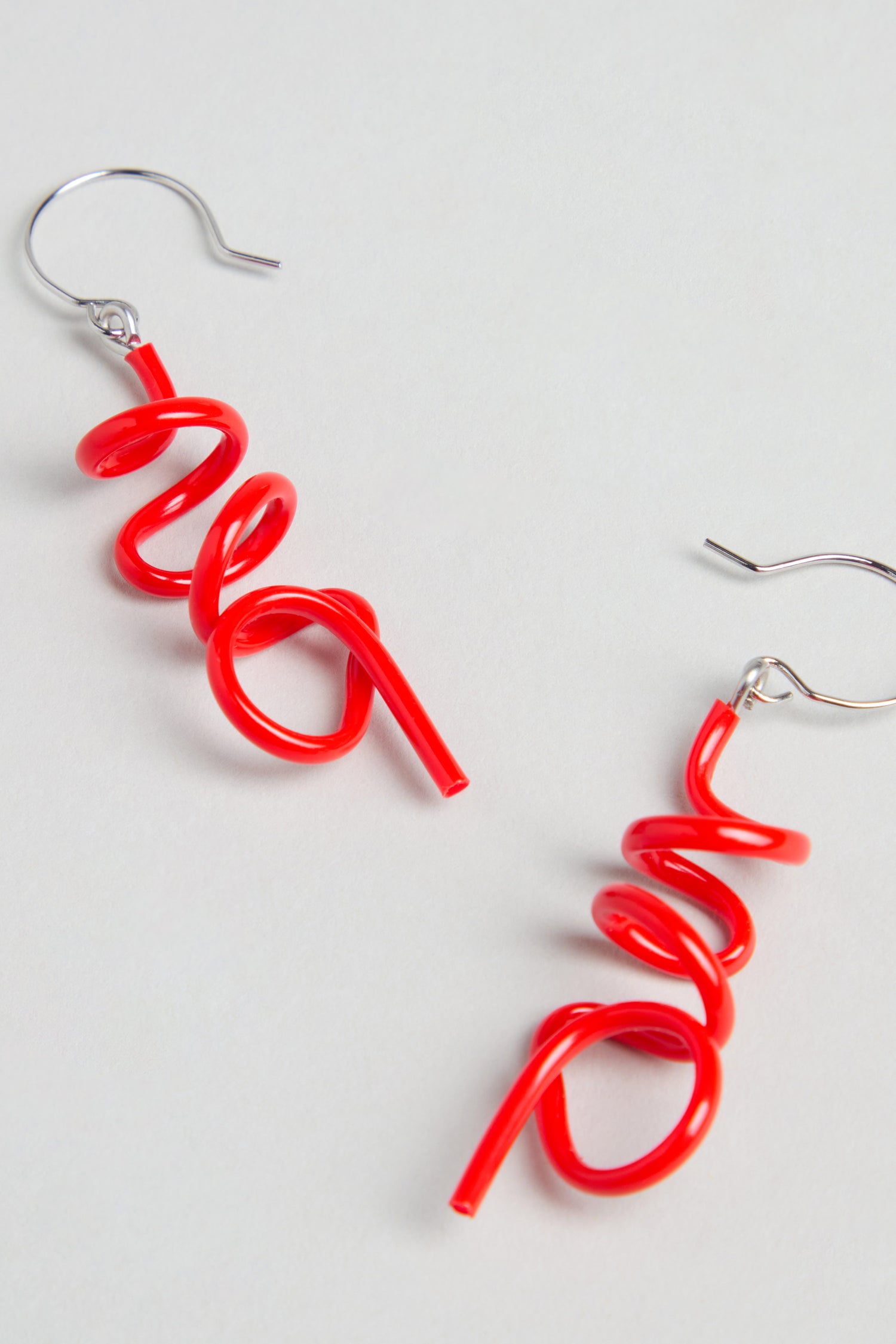 The Mini Sketch Earrings feature bright red, spiral-shaped dangles on silver hooks. Handmade in Paris, they're perfect for lovers of colourful jewellery and are shown displayed against a light background.