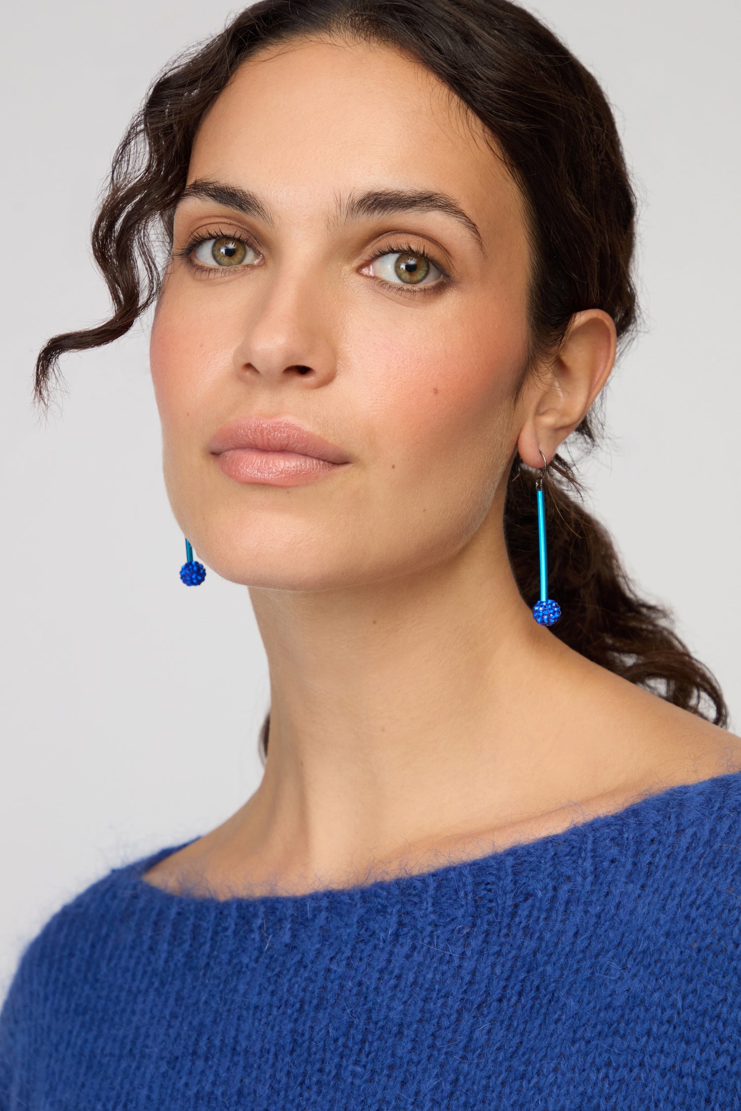 Woman with wavy brown hair wears a blue sweater and Samuel Coraux’s contemporary Disco Ball Earrings, posing against a plain background and looking directly at the camera.