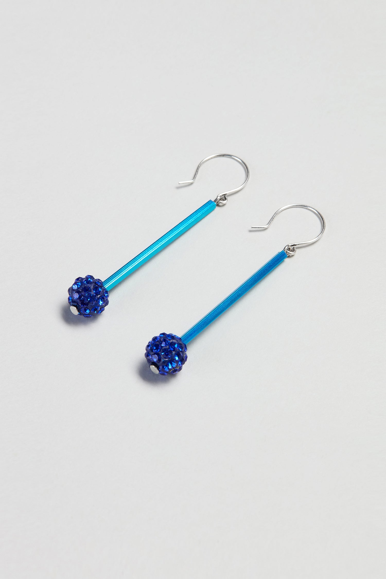 The Samuel Coraux Disco Ball Earrings feature blue rods and dark blue beaded spheres, making a bold statement in contemporary jewellery. Displayed on a light background, these dangle earrings are truly eye-catching.