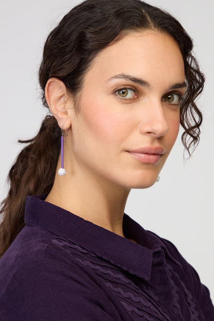 Woman with wavy dark hair in a ponytail, wearing a purple collared shirt and Disco Ball Earrings, looks at the camera with a neutral expression.