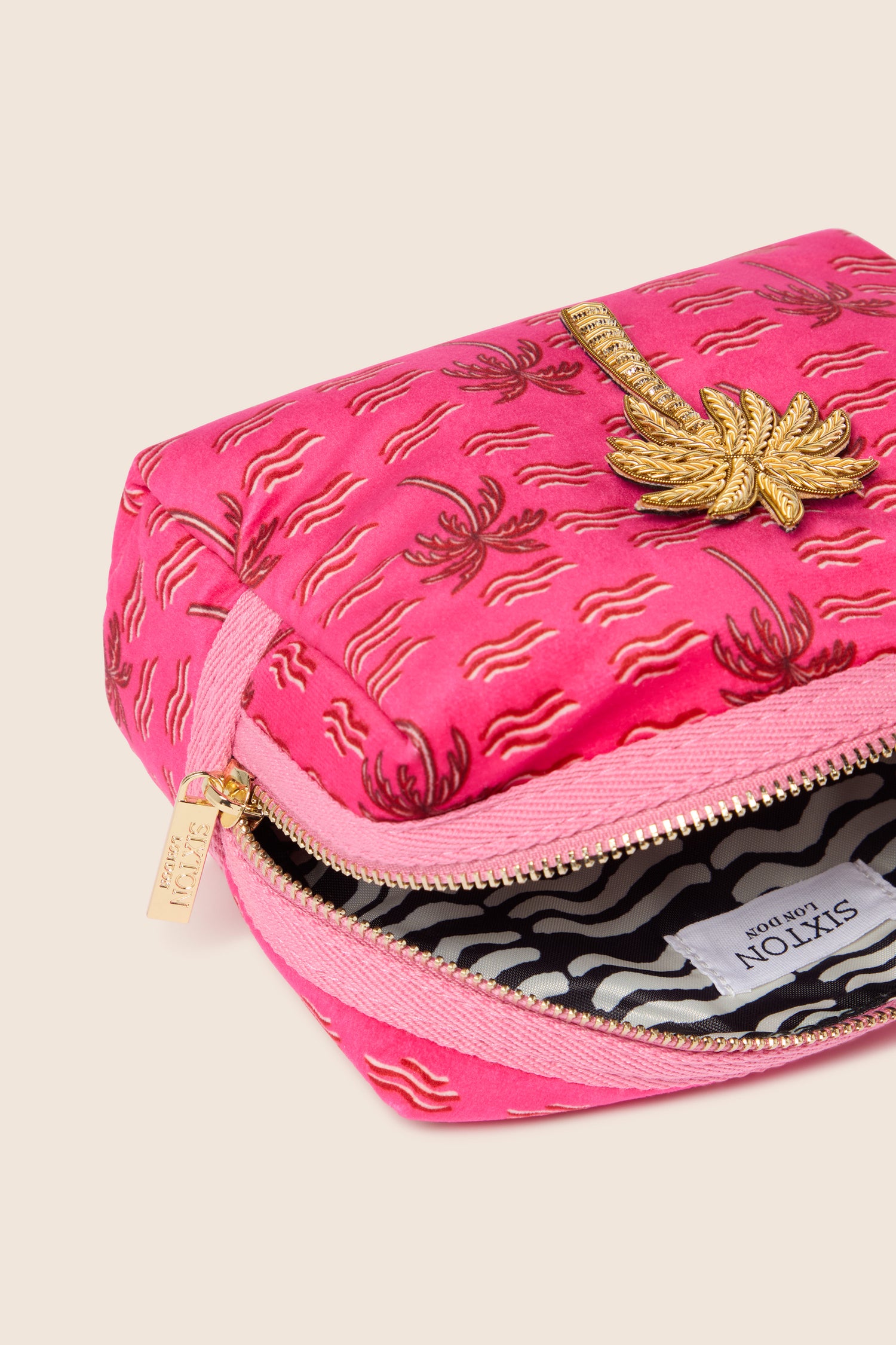 Introducing the Large Palm Make-Up Bag, a touch of tropical elegance with its pink exterior adorned with gold palm tree design embroidery, complemented by a gold zipper and a black-and-white patterned interior lining.