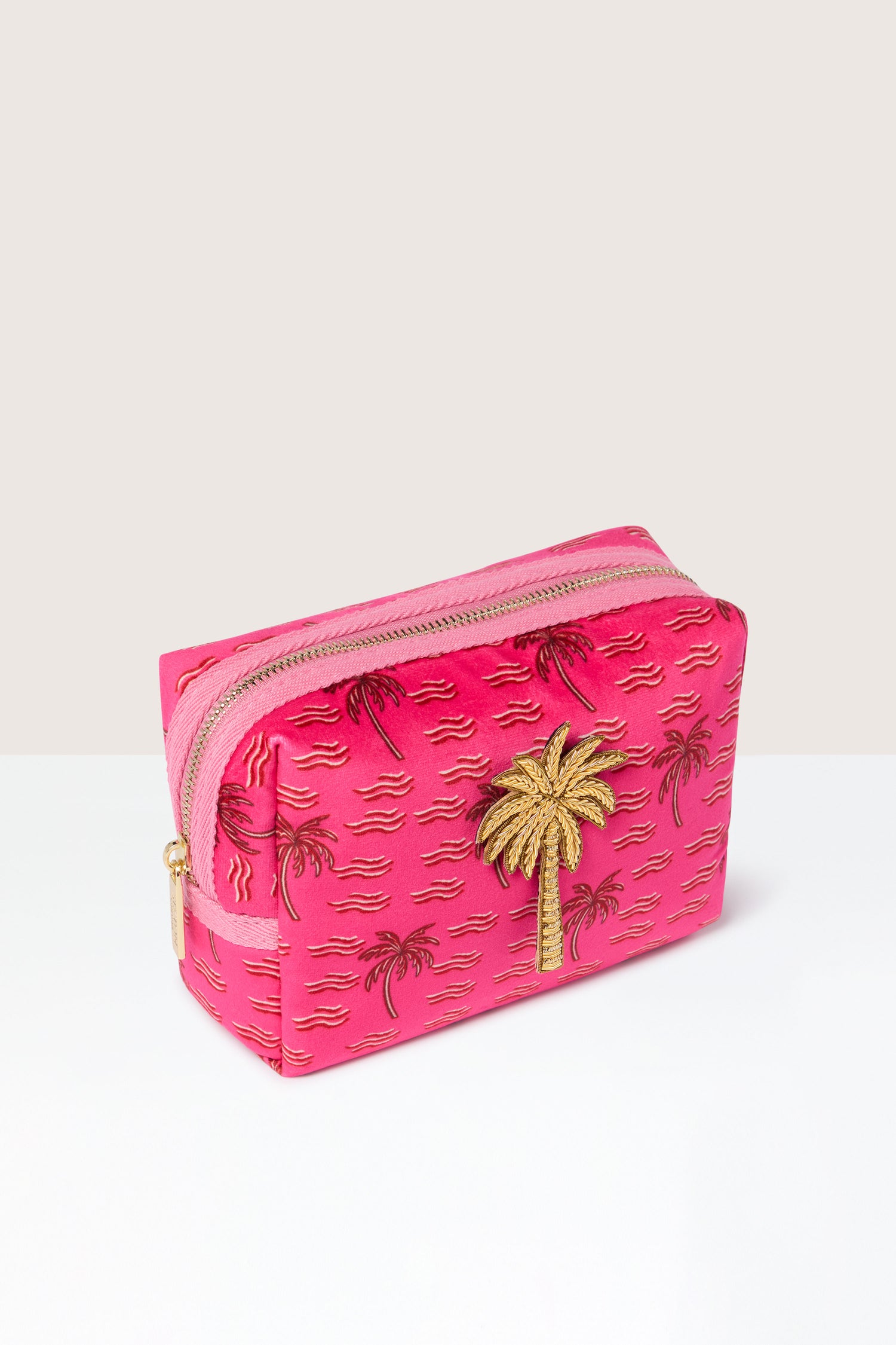The Large Palm Make-up Bag, featuring a sophisticated gold palm tree design and a convenient zipper closure, stands on a white surface against a beige background, exuding tropical elegance.