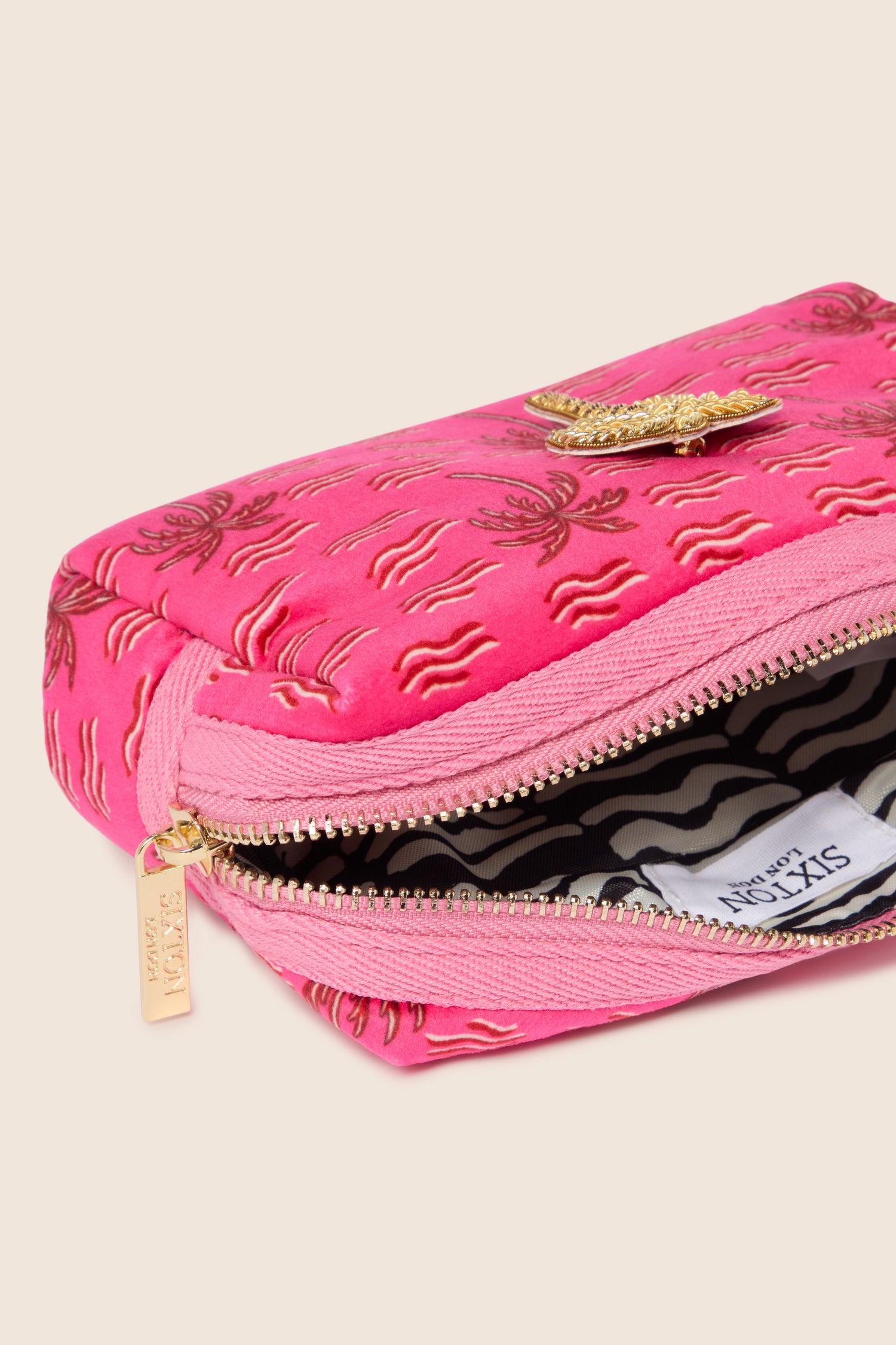 The Small Palm Make-Up Bag showcases a stylish pink zippered pouch adorned with elegant gold embroidery and a matching gold clasp. Inside, you'll find a chic black-and-white striped pattern, ideal for organizing your beauty essentials while infusing tropical vibes into your daily routine.