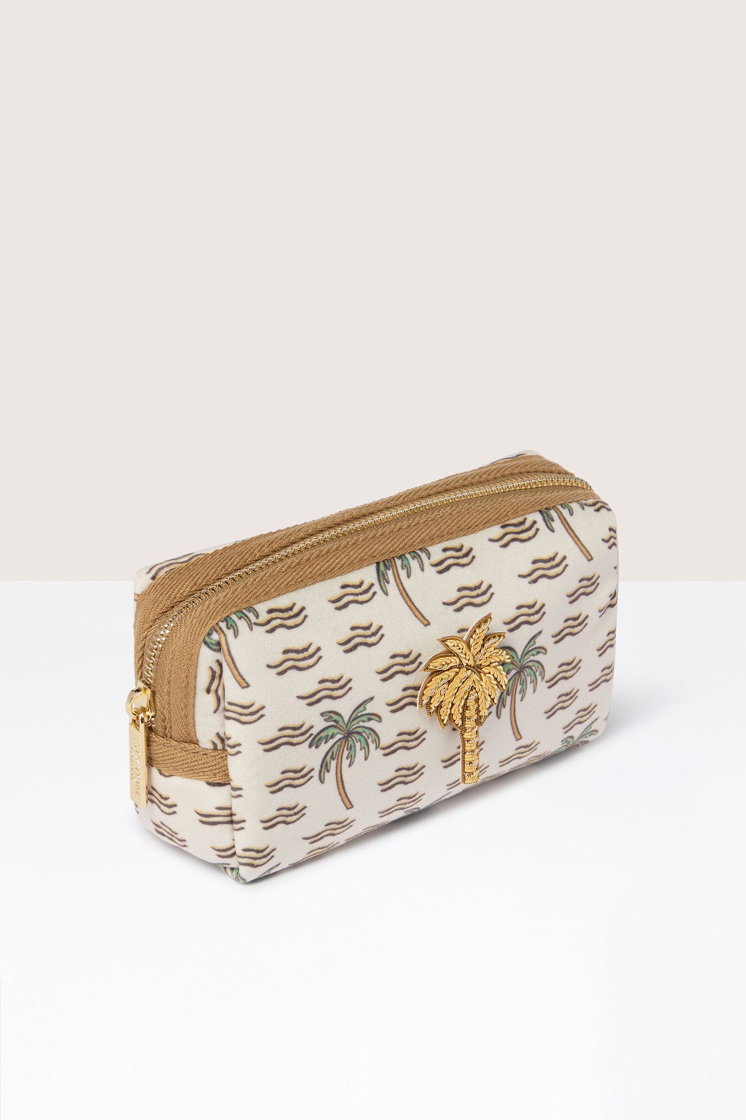 The Small Palm Make-Up Bag, a beige zippered pouch adorned with a palm tree pattern and a small golden palm tree embellishment on the front, is perfect for storing your beauty essentials and exudes tropical vibes.