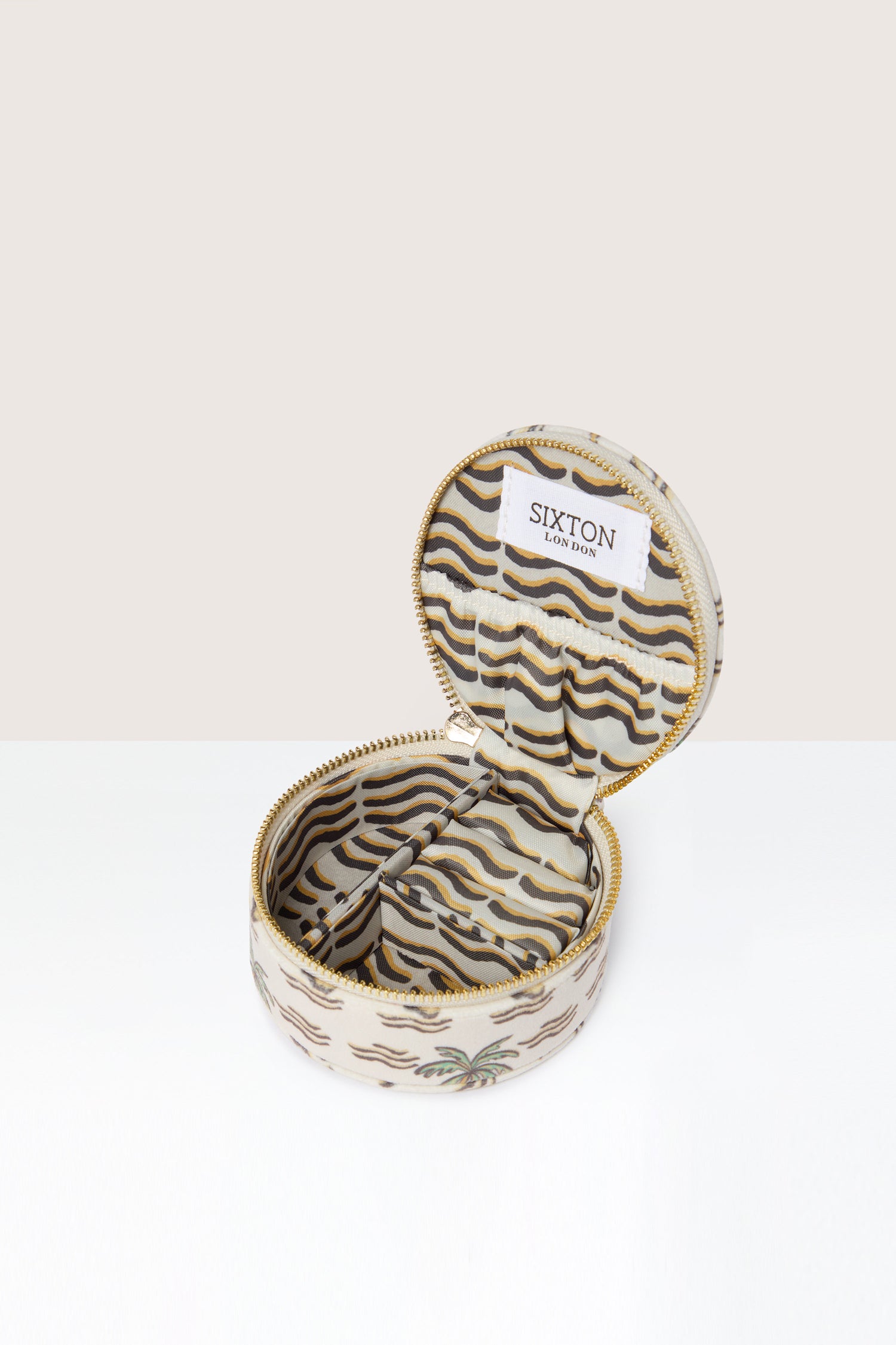 A small, round Palm Jewellery Travel Pot with a white and gold wavy pattern, open to reveal its zebra print lining and a label with text reading "SIXTON LONDON.