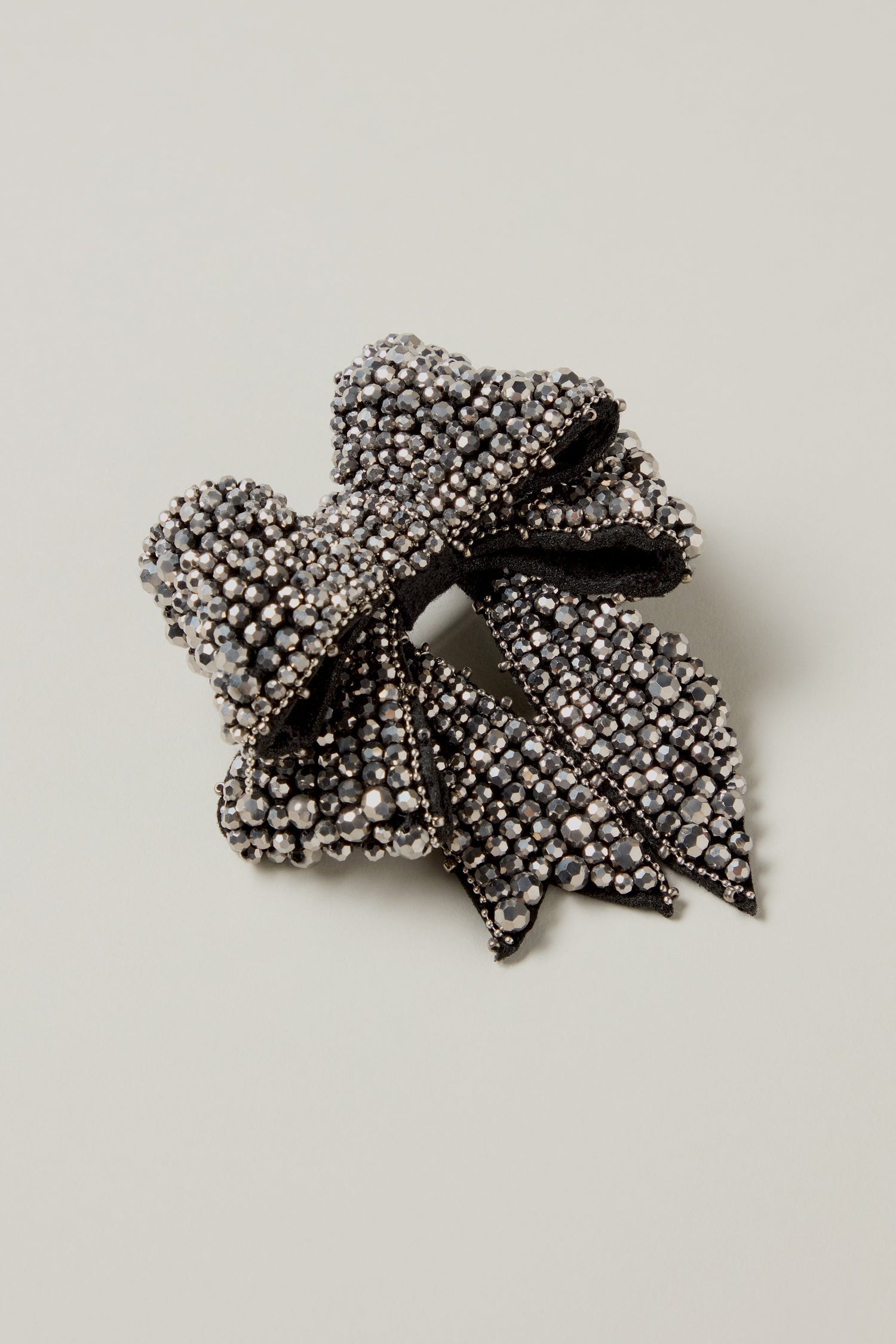 The Hand Beaded Bow Brooch is a black fabric hair clip adorned with small, shiny silver rhinestones, photographed against a plain light background.