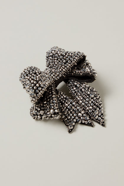 The Hand Beaded Bow Brooch is a black fabric hair clip adorned with small, shiny silver rhinestones, photographed against a plain light background.
