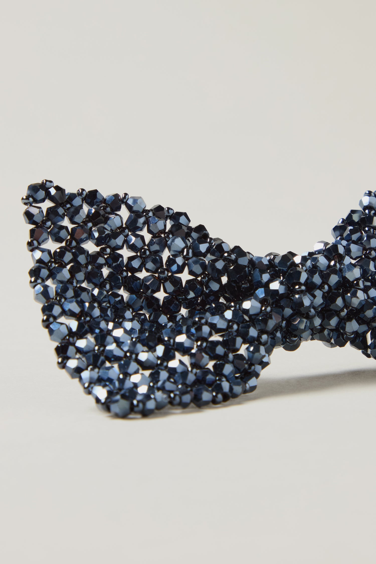A close-up of the Hand Beaded Bow Tie Brooch in dark blue, adorned with numerous small, shiny beads, shown against a plain background.