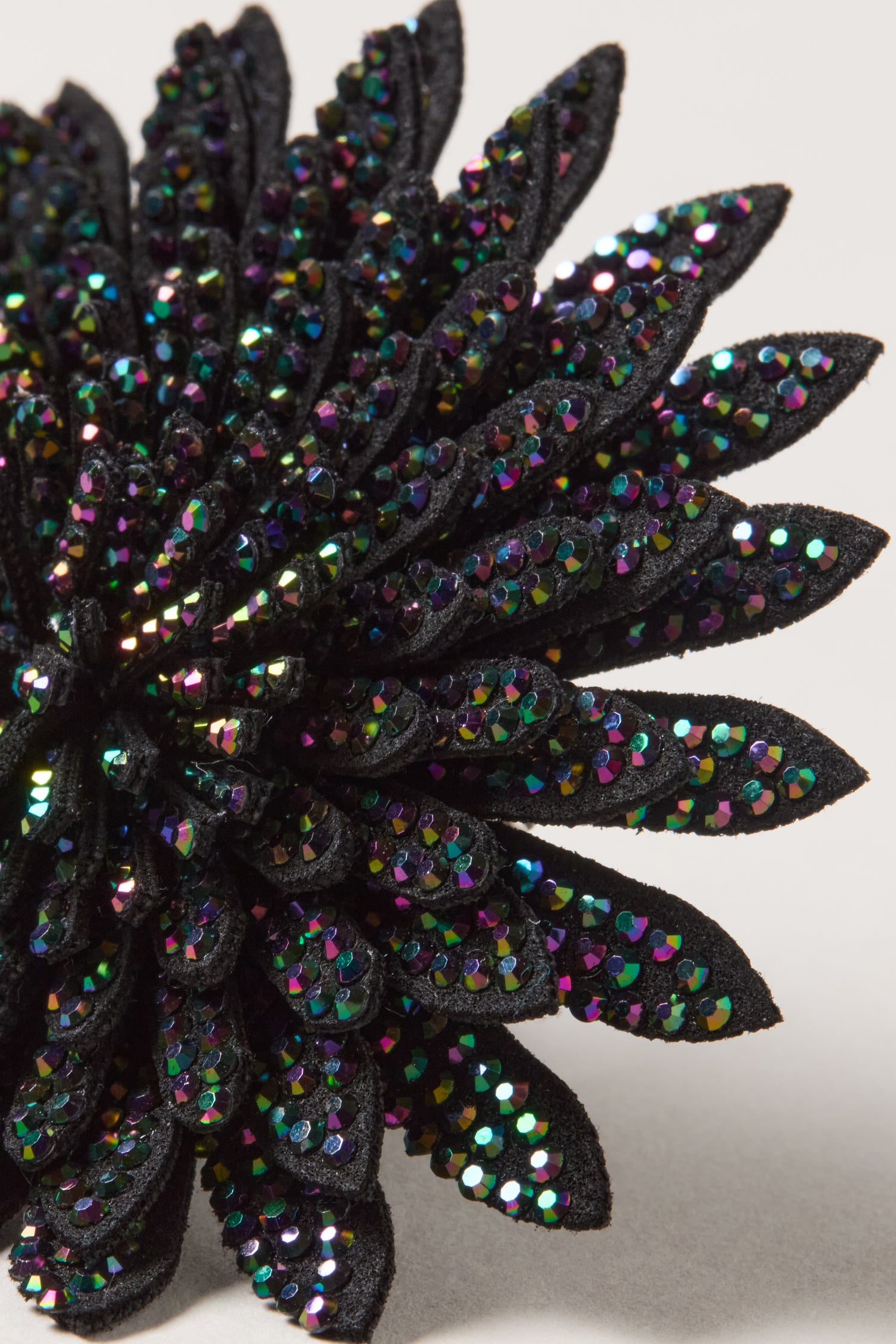 Close-up of the Dahlia Flower Brooch featuring black layered petals embellished with multicolored iridescent sequins, creating a striking floral accessory set against a neutral background.
