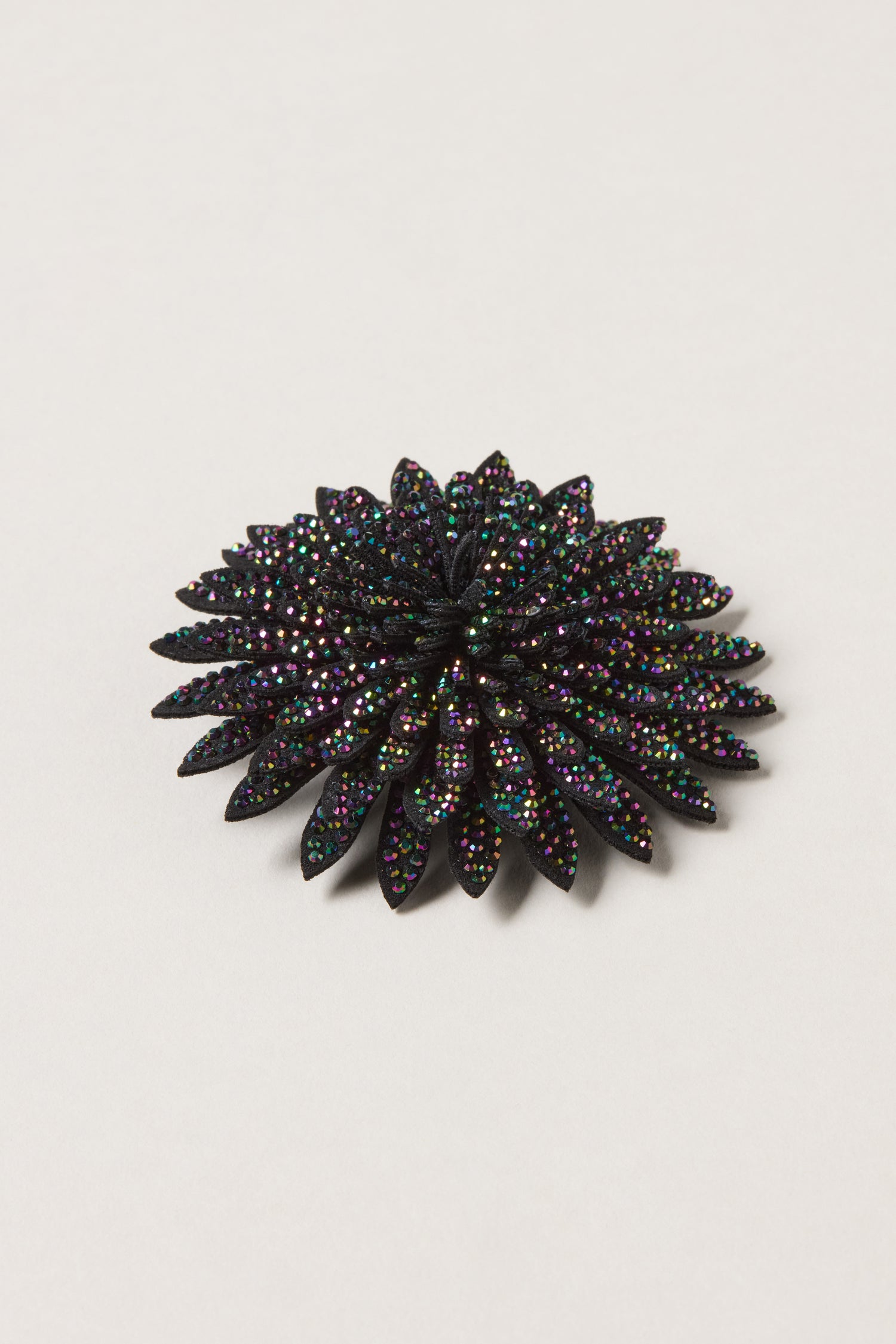 The Dahlia Flower Brooch is a stunning black beaded accessory, inspired by dahlia petals and embellished with multicolored sparkling rhinestones, shown against a plain white background.