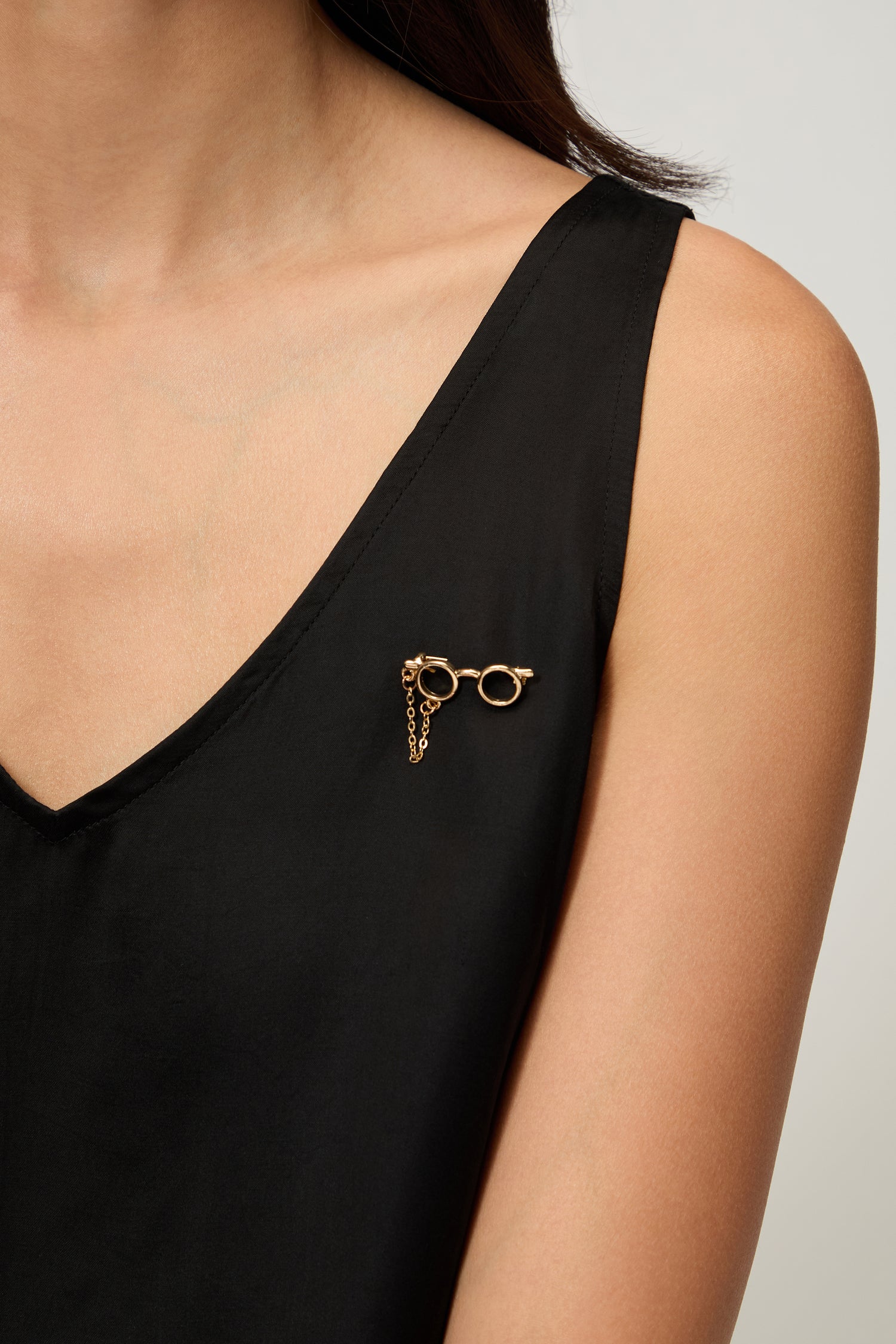 A person in a black sleeveless top wears a playful Spectacles Brooch pinned near the left shoulder.