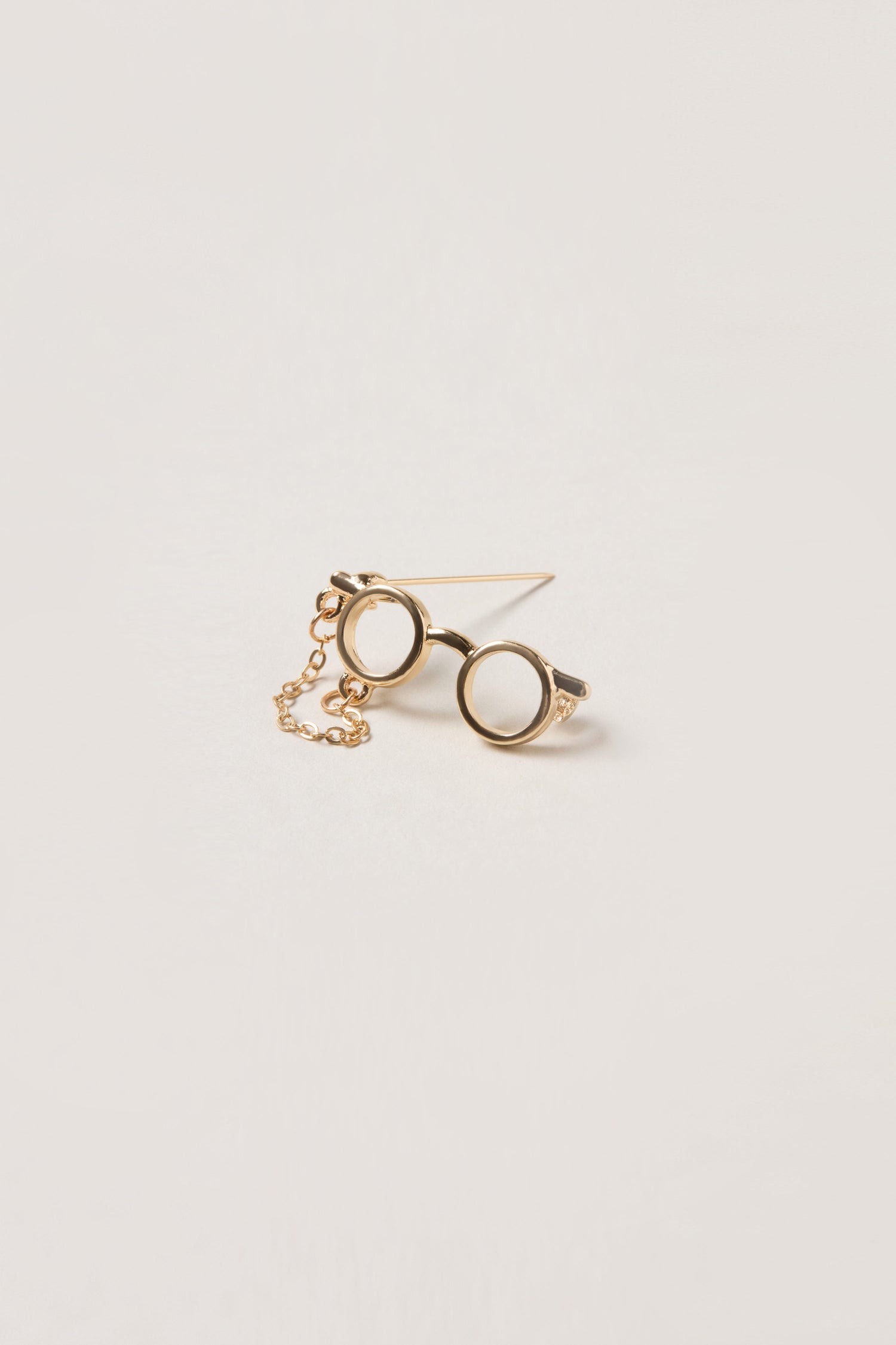 A whimsical accessory, the Spectacles Brooch is shaped like round eyeglasses with a delicate chain, shown against a neutral background.