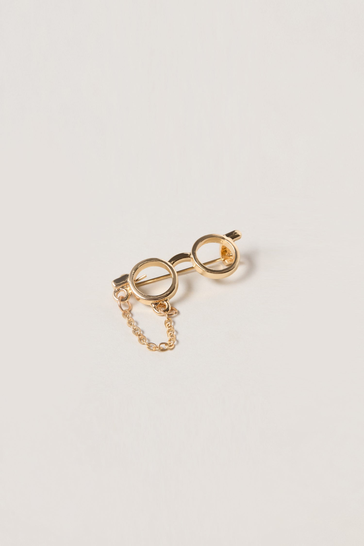 A whimsical accessory, the Spectacles Brooch features two circular ends connected by a short chain, showcased against a plain white background.