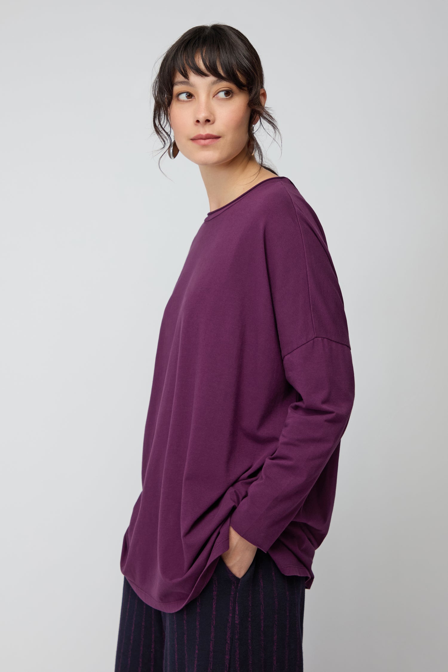 A person wears the Cotton Jersey Relaxed Top with dark pants, one hand in their pocket and looking to the side—highlighting this comfortable wardrobe essential.