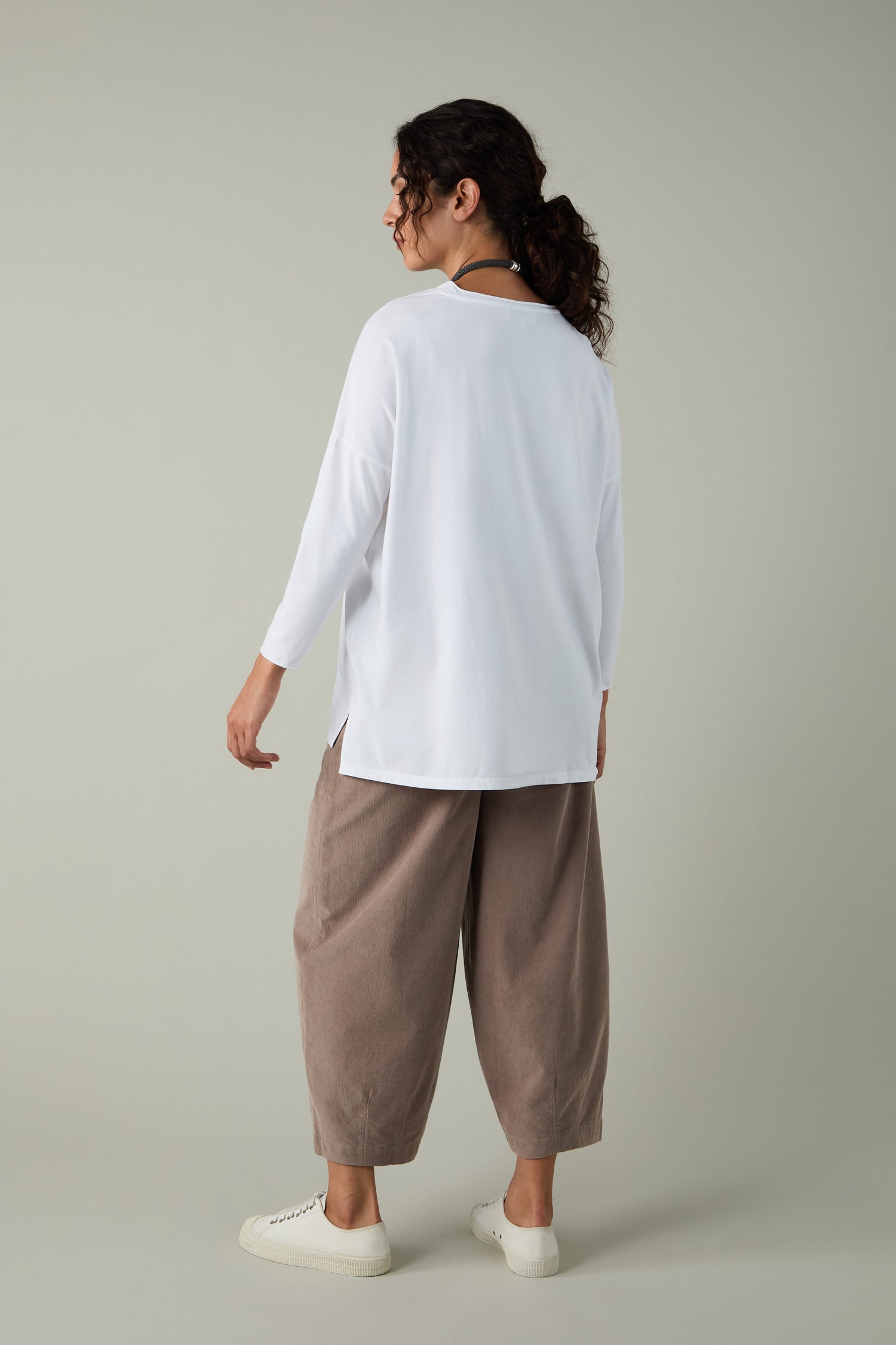 A person stands facing away, wearing the Cotton Jersey Relaxed Top with a comfortable fit, taupe wide-leg pants, and white sneakers against a plain light gray background.