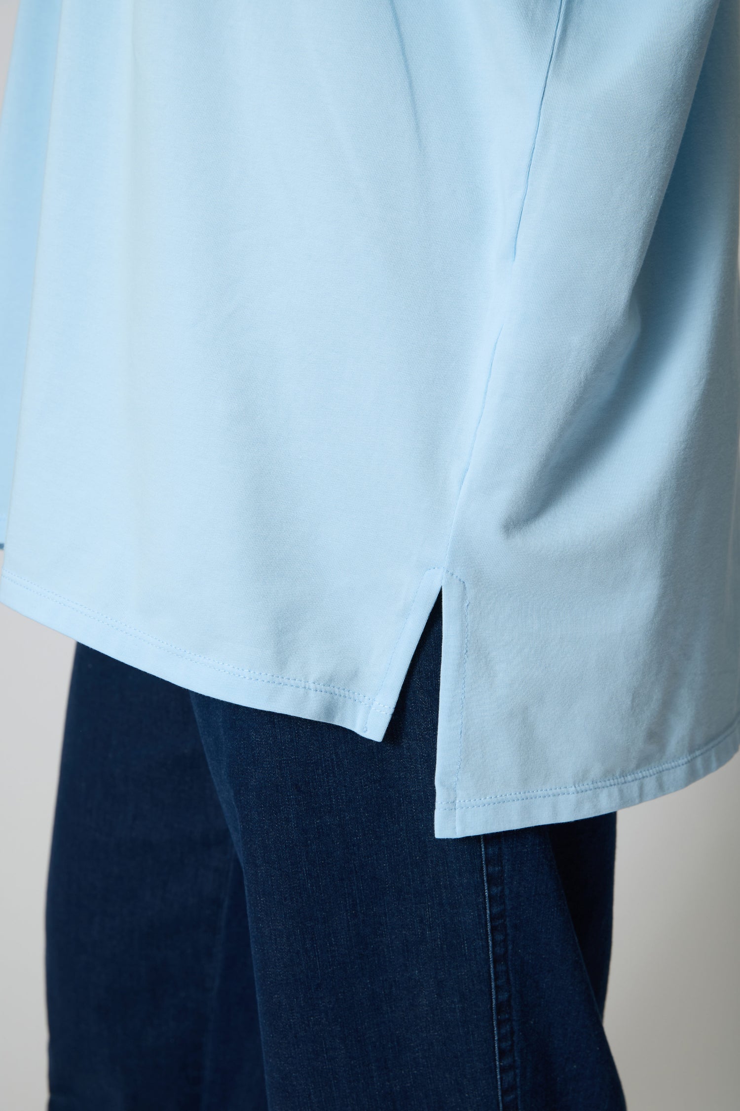 Close-up of a person wearing the Cotton Jersey Relaxed Top in light blue with a side slit, styled with dark blue denim jeans.