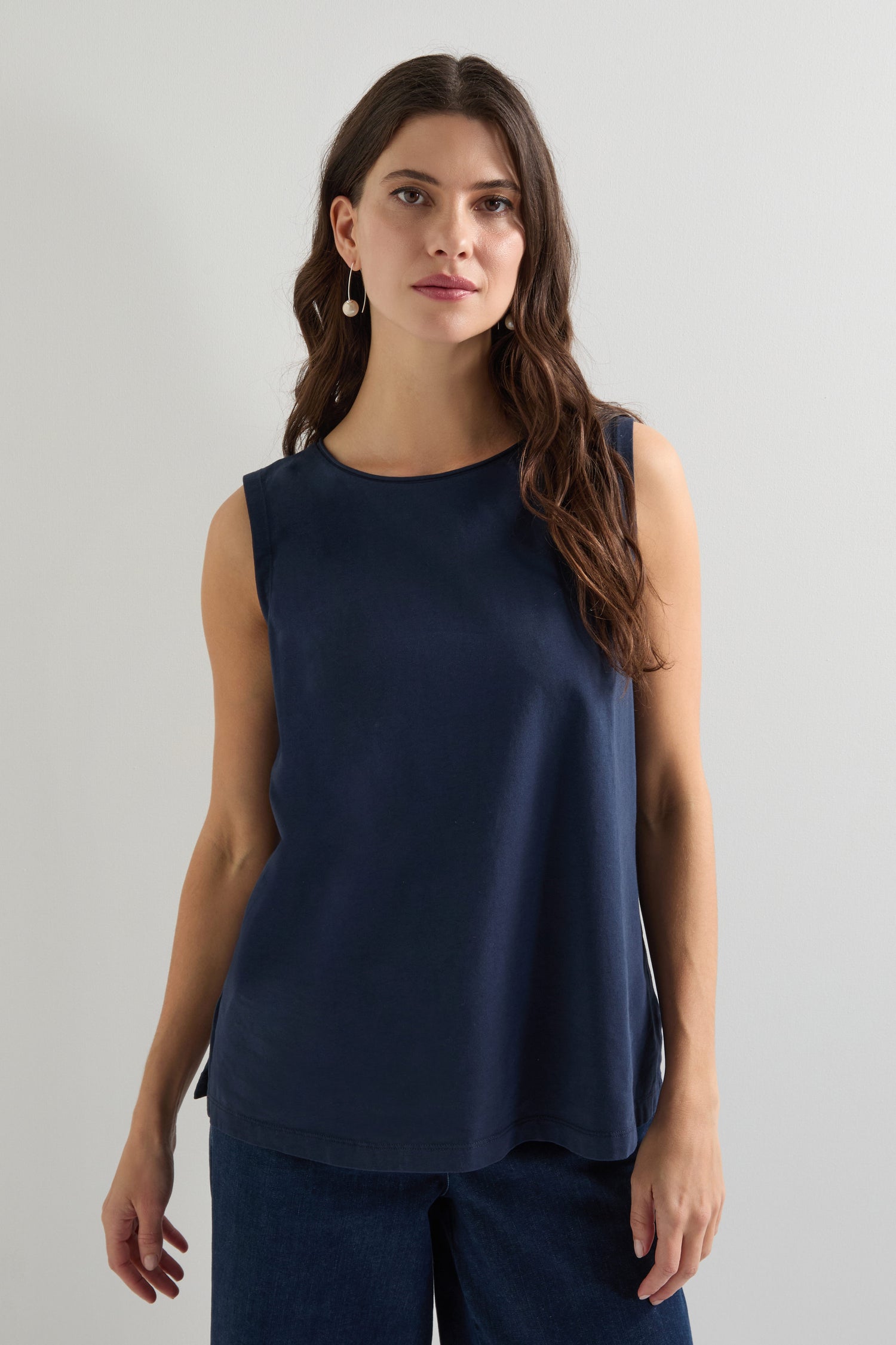 A woman with long brown hair wears a Cotton Jersey Boxy Vest in navy, a relaxed-fit and sleeveless top made from breathable stretch jersey, along with dark pants, set against a plain white background.