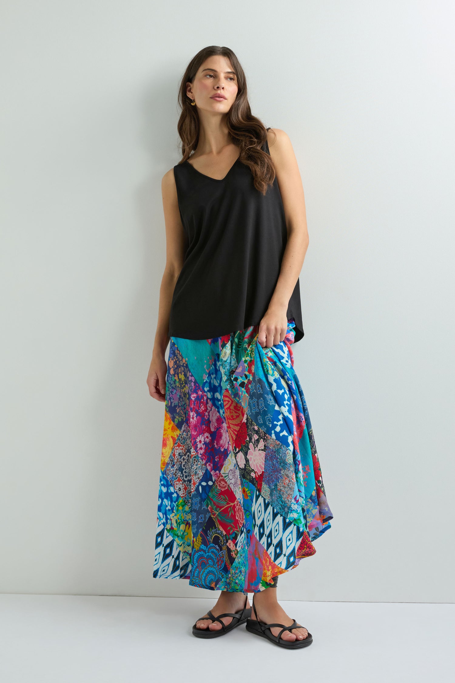Woman stands against a plain wall wearing the Viscose Jersey V Neck Vest, a colorful patchwork maxi skirt, and black sandals.