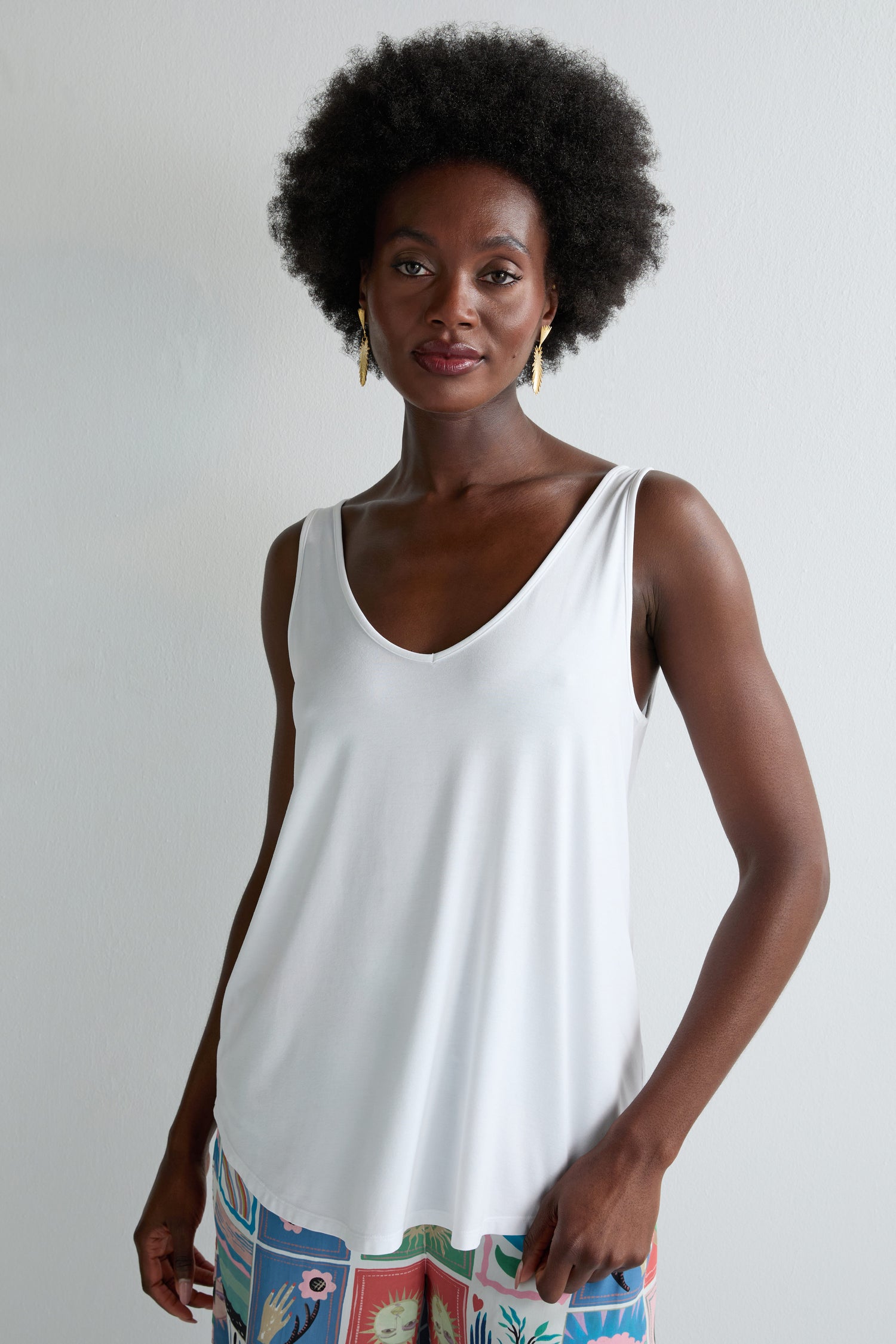 A woman with an afro hairstyle wears the Viscose Jersey V Neck Vest and colorful patterned pants, perfect for summer, standing against a plain light-colored background.