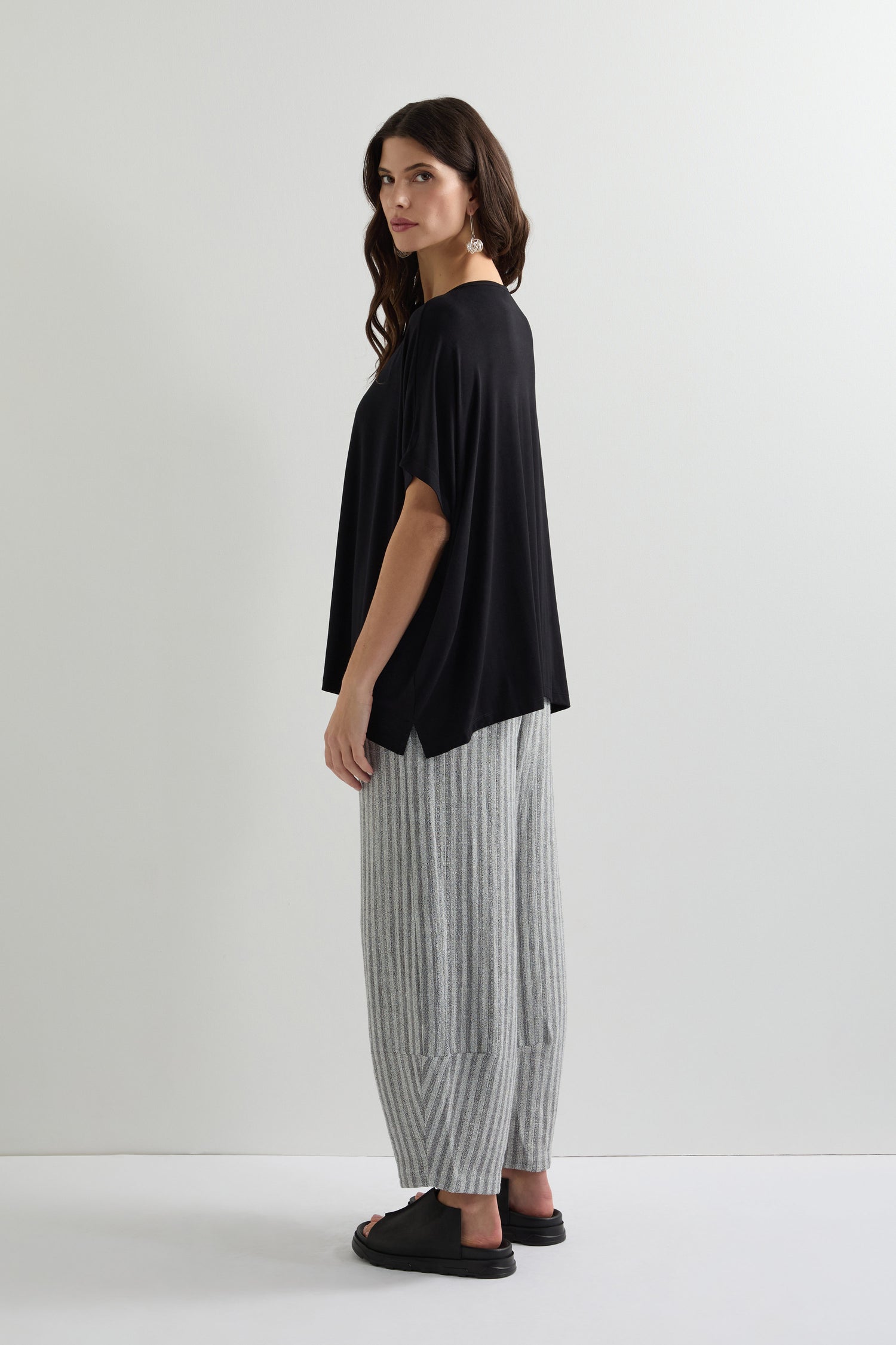 A woman effortlessly showcases everyday dressing with a Viscose Jersey Square Top, gray striped wide-leg pants, and chic black sandals as she stands sideways against a white background.