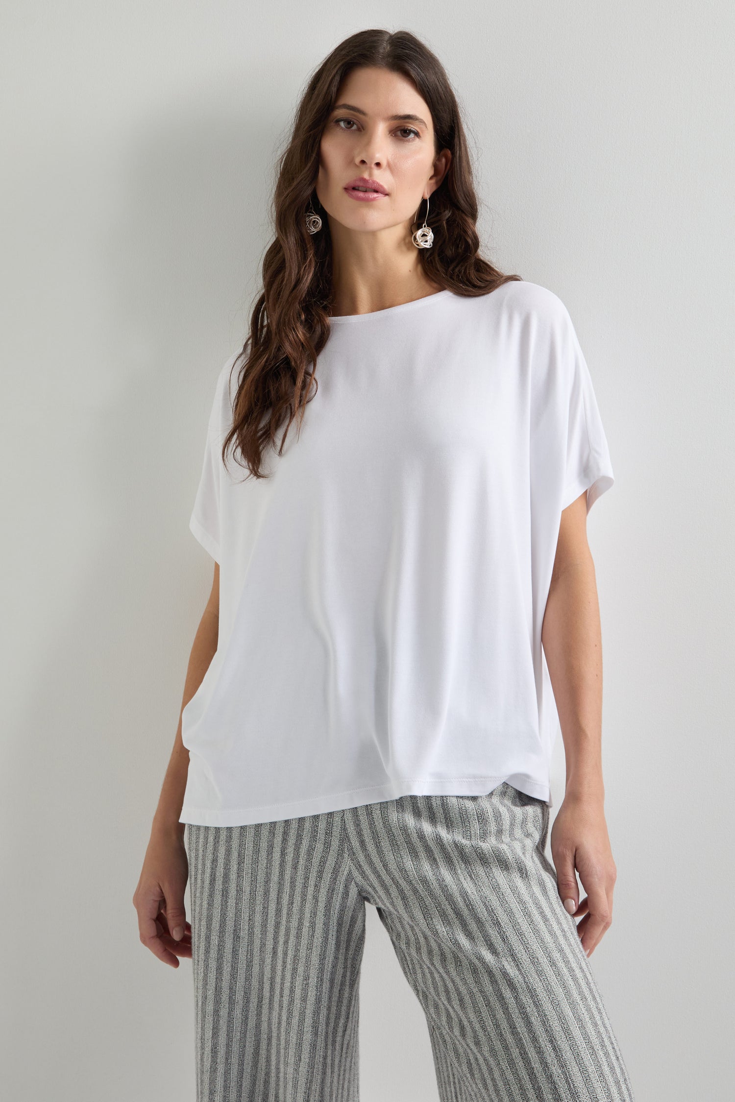 A woman wears a Viscose Jersey Square Top, beautifully paired with striped gray pants against a plain backdrop, showcasing the essence of everyday style.