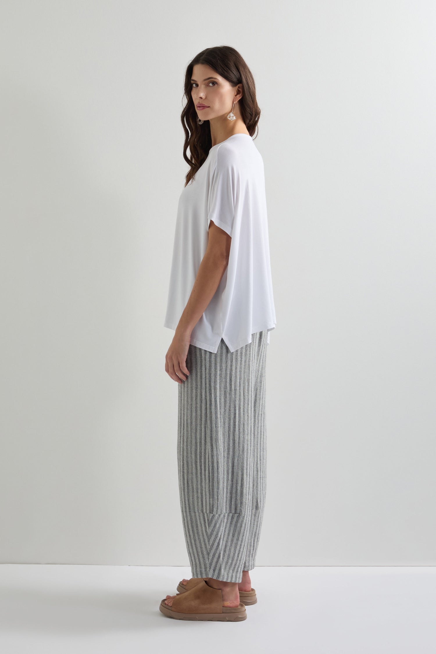 A woman stands sideways, wearing a white Viscose Jersey Square Top and gray striped pants on a plain background. This outfit is perfect for everyday dressing, combining comfort and style seamlessly.