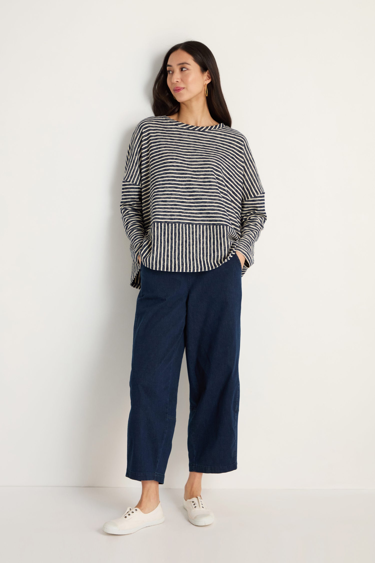 A woman stands against a white wall wearing the Textured Stripe Jersey Boxy Top, wide-leg dark blue pants, and white sneakers.