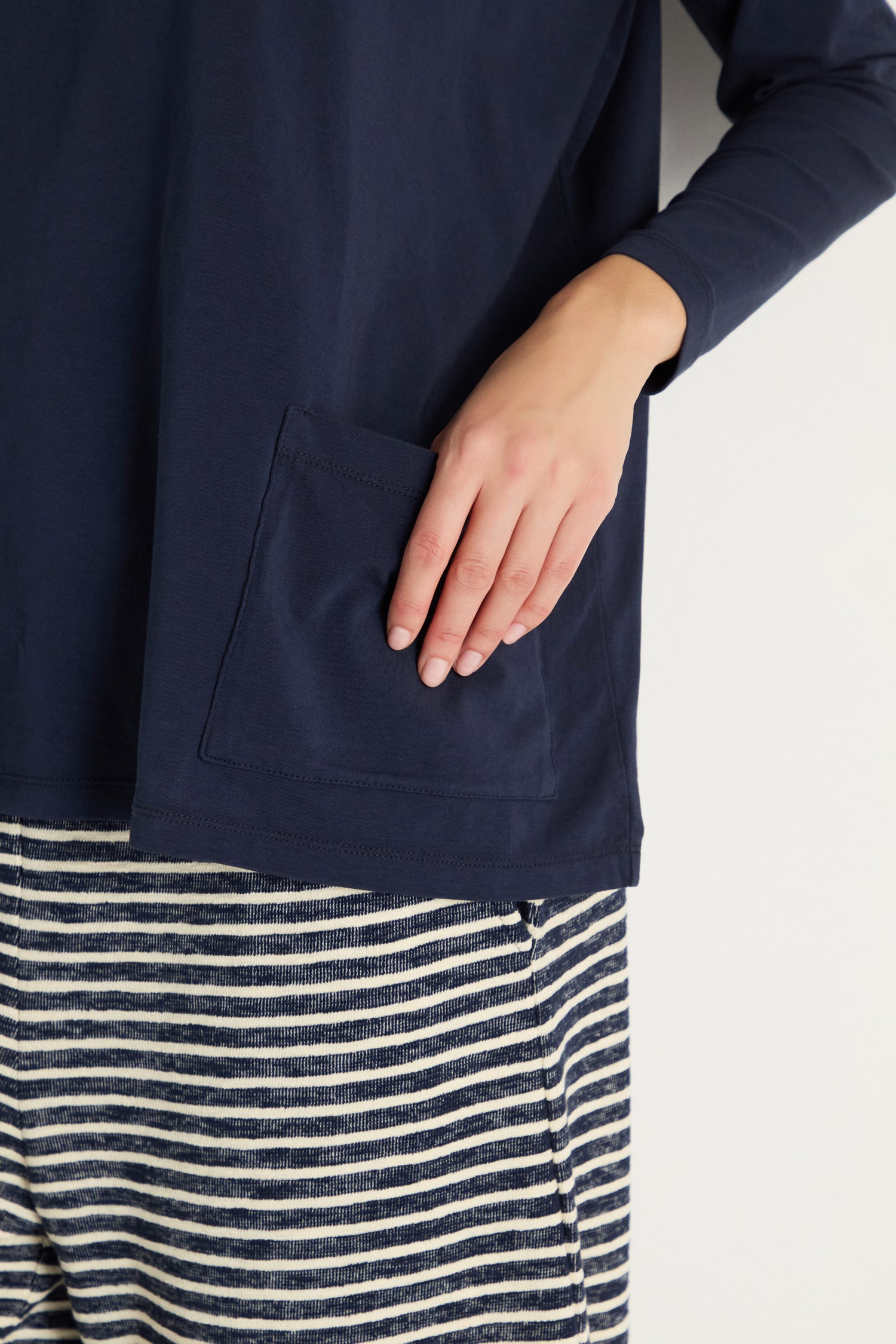 A person wearing the Cotton Jersey Boxy Pocket Top in navy and striped navy and white pants places their hand inside the pocket.