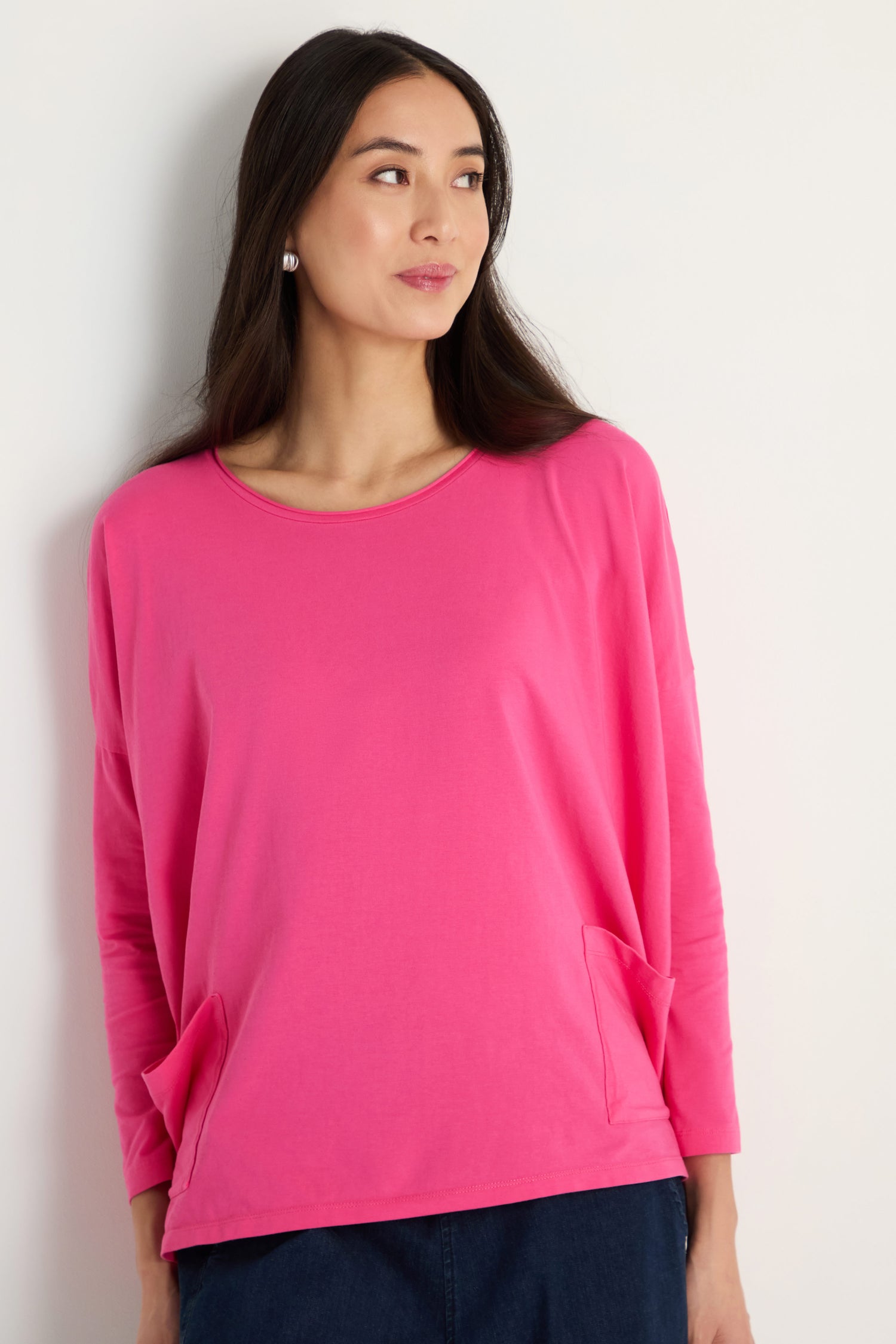 A woman with long dark hair models the Cotton Jersey Boxy Pocket Top in bright pink, featuring an oversized fit and two front pockets, against a plain white background.