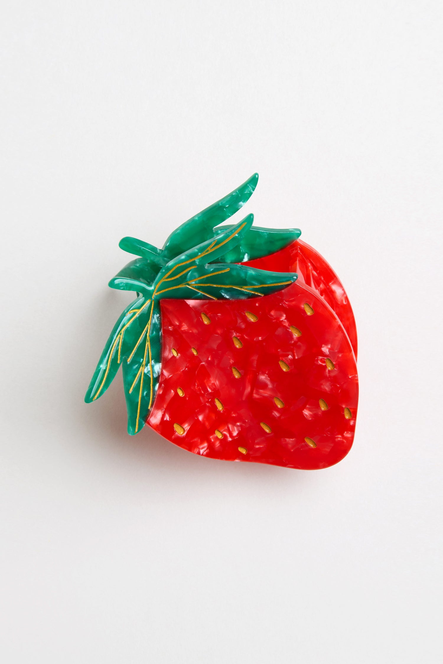 A glossy, marbled Hand Painted Strawberry Hair Clip shaped like a red strawberry with green leaves is shown on a plain white background.