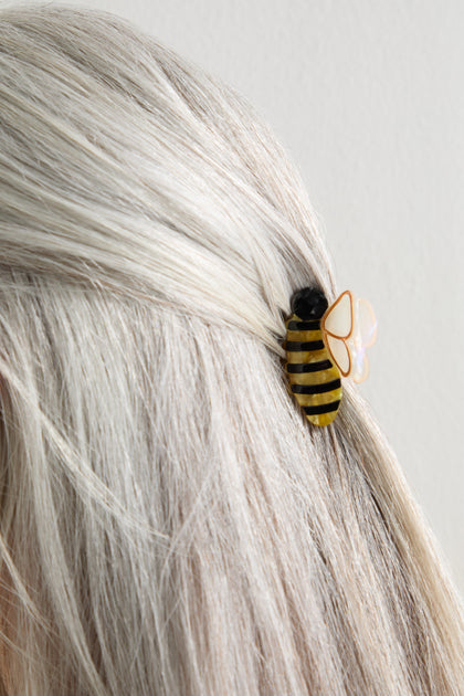 Close-up of light blonde hair pinned back with a Hand-Painted Mini Bee Hair Clip, showcasing yellow and black stripes, marbled amber accents, and opalescent wings.