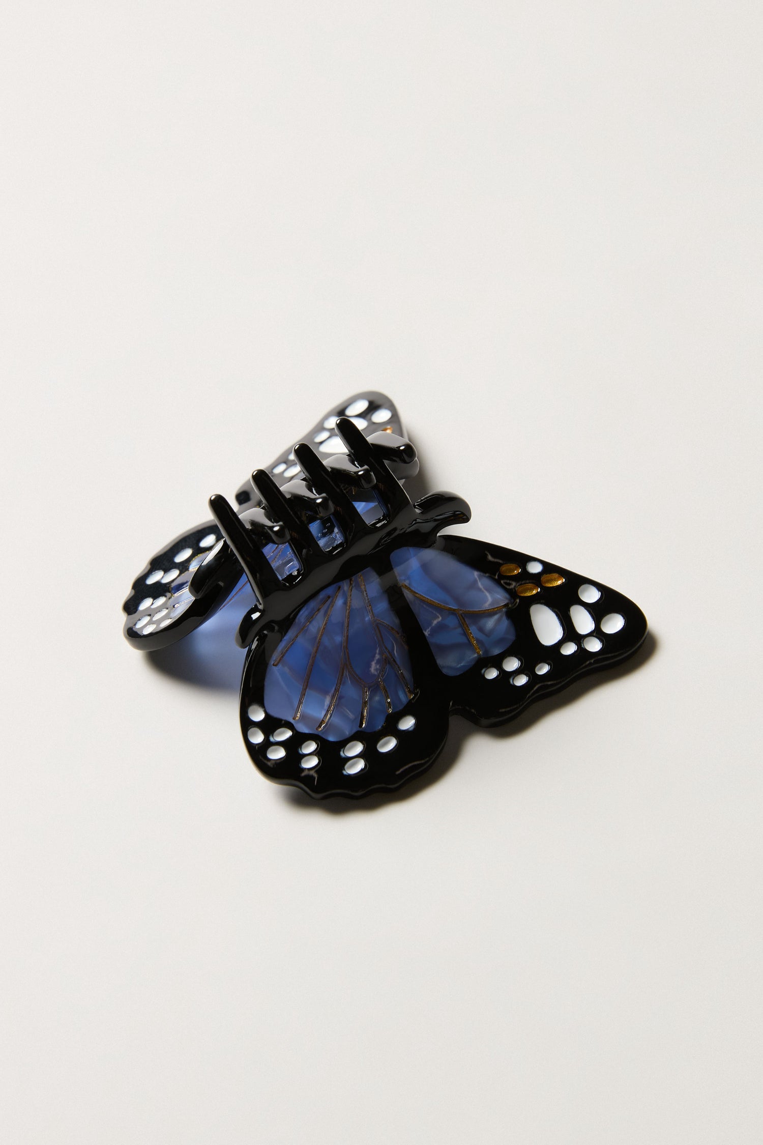 The Hand-Painted Mini Monarch Butterfly Hair Clip, featuring black and blue wings with cut-out monarch-inspired details, is displayed on a plain white background.