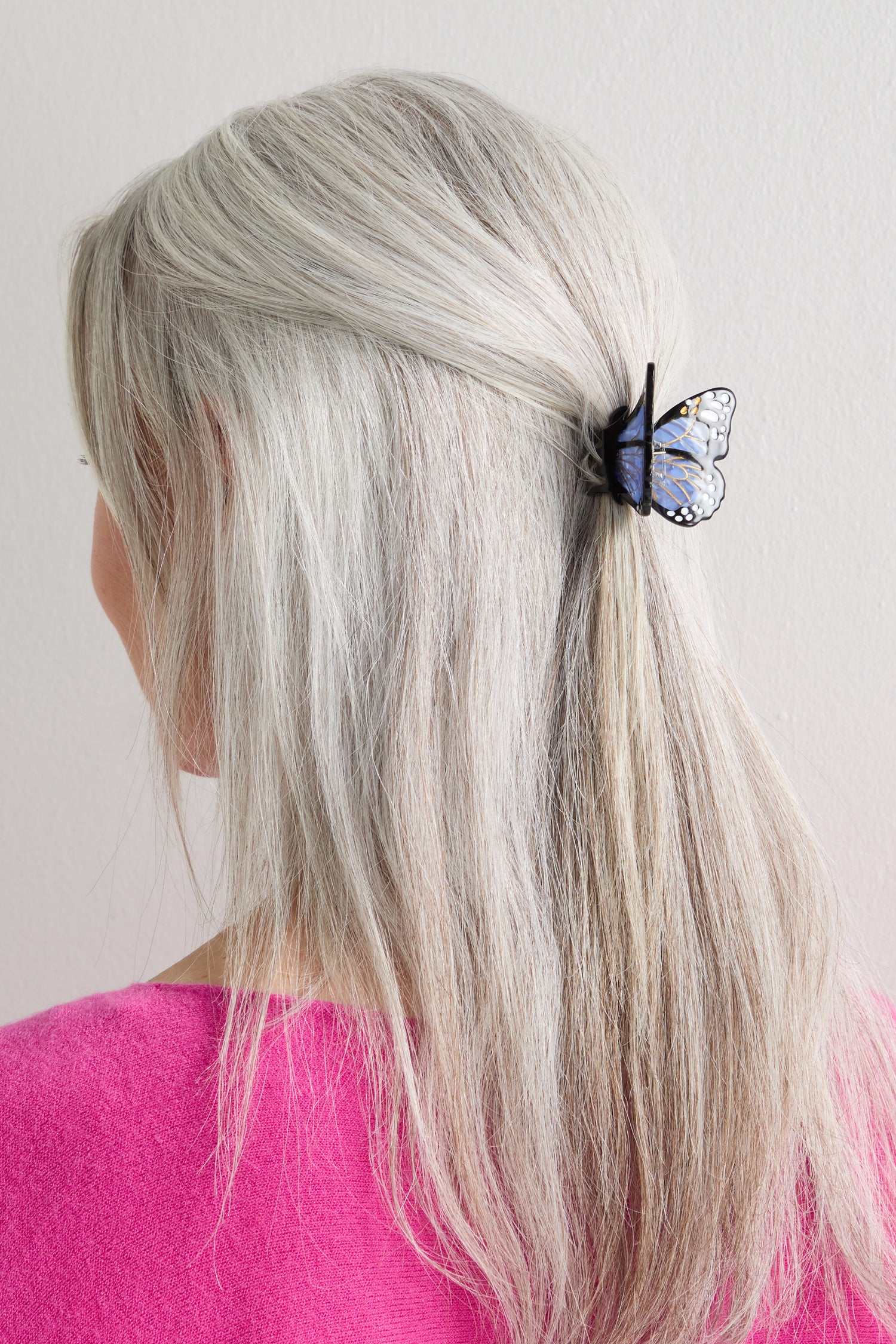 A person with long, straight gray hair, wearing a pink top, has a Hand-Painted Mini Monarch Butterfly Hair Clip securing part of their hair at the back.