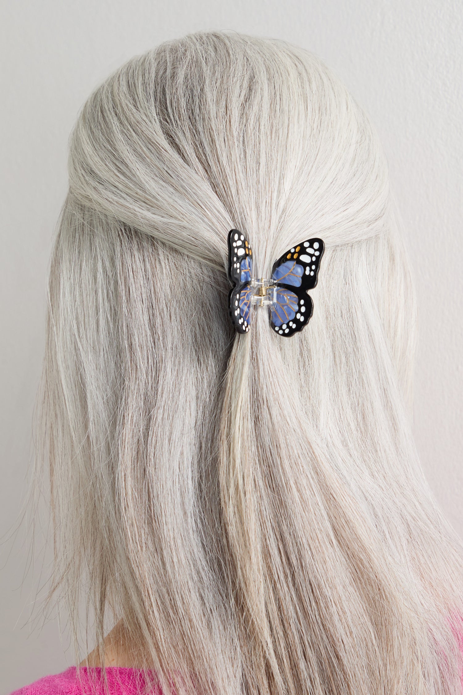 A person with long, straight, gray hair is seen from behind wearing a Hand-Painted Mini Monarch Butterfly Hair Clip with a black and orange monarch wing pattern.