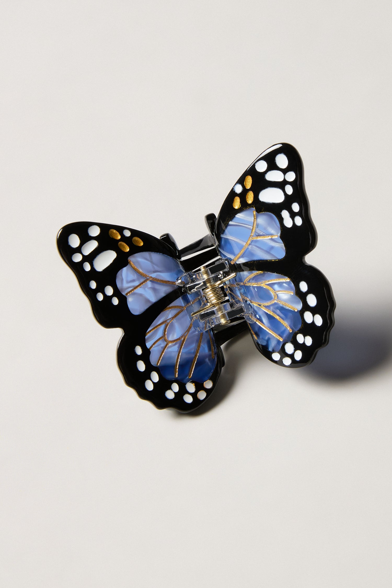 A Hand-Painted Mini Monarch Butterfly Hair Clip, showcasing black, blue, and gold wing patterns, is displayed against a plain light background.