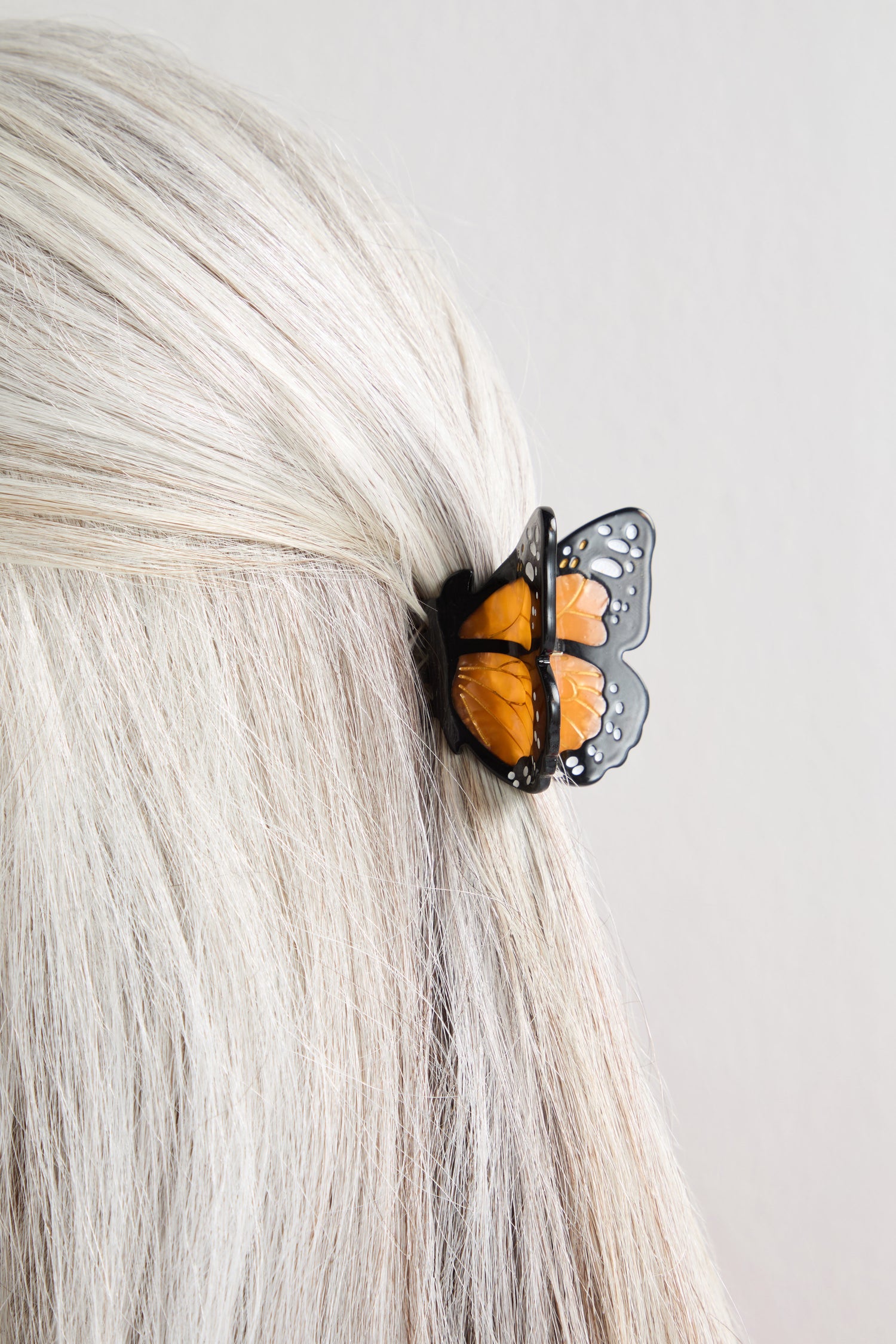 A close-up of light blonde hair styled with the Hand-Painted Mini Monarch Butterfly Hair Clip, featuring a detailed orange and black monarch wing design.