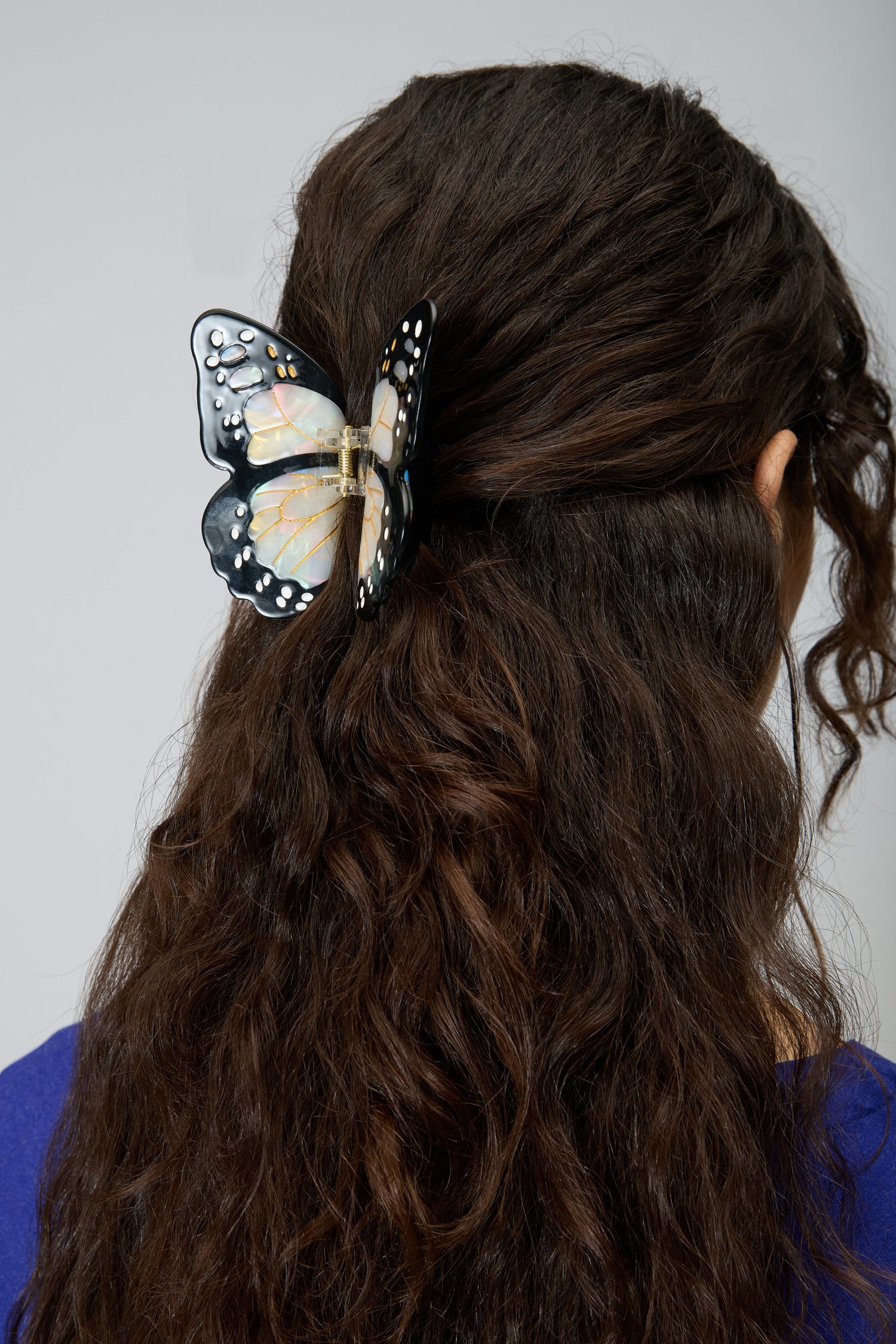 A person with long, wavy brown hair wears the Hand Painted Monarch Butterfly Hair Clip, adding an eco-friendly accent to their style.