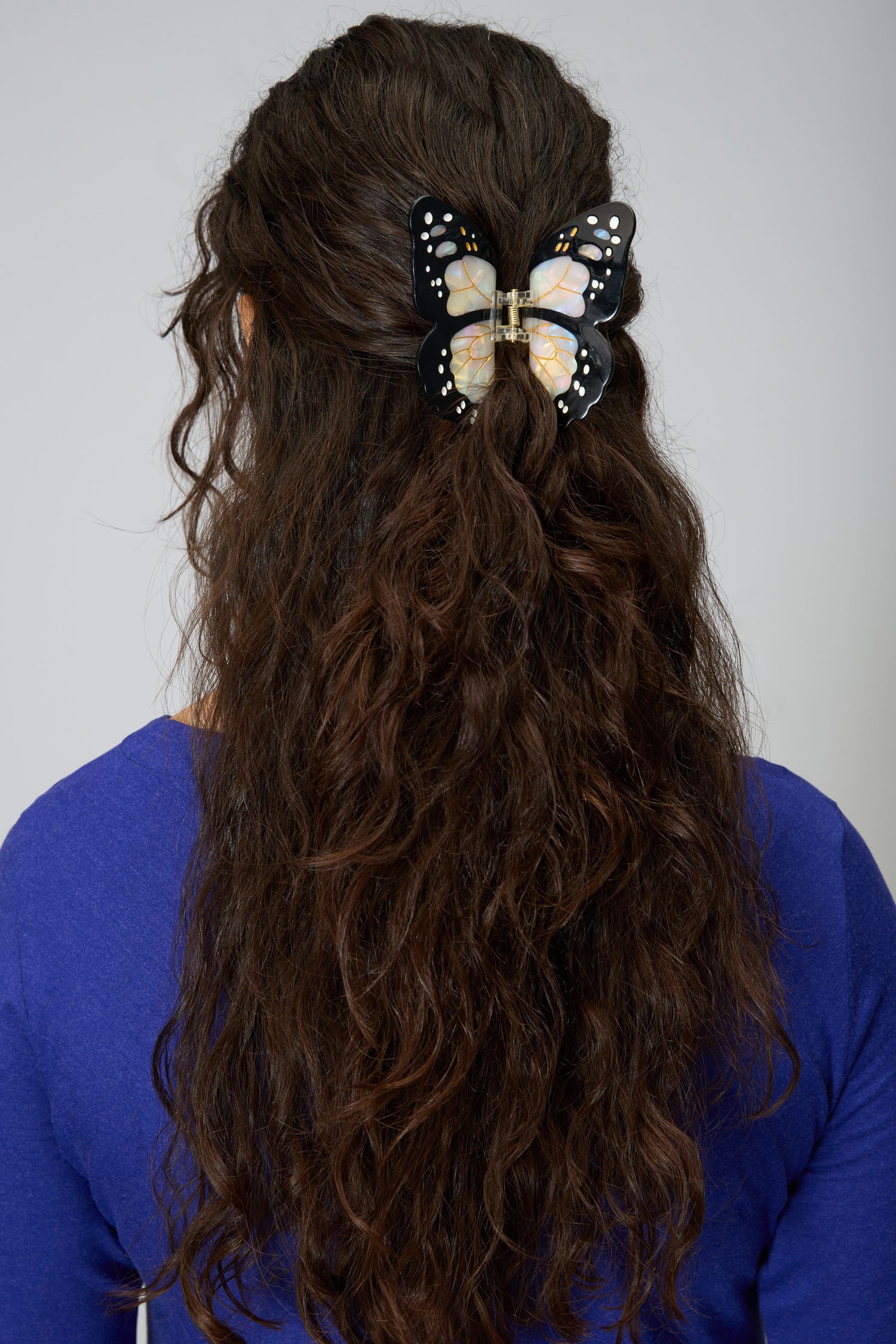 A person with long, wavy brown hair is shown from the back wearing a blue top and the Hand Painted Monarch Butterfly Hair Clip.