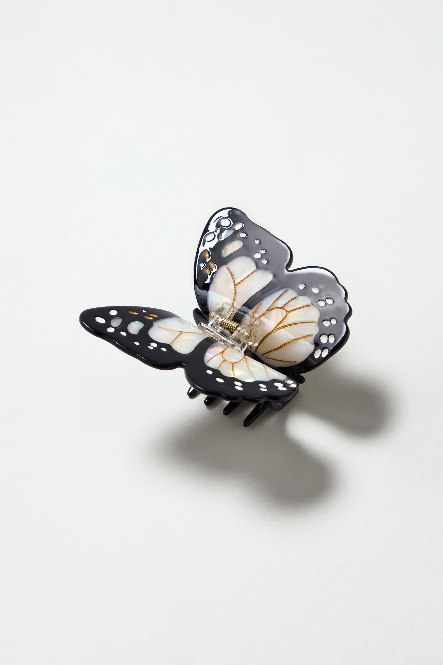 The Hand Painted Monarch Butterfly Hair Clip, featuring black, white, and yellow details in a butterfly shape, is displayed on a light gray surface.