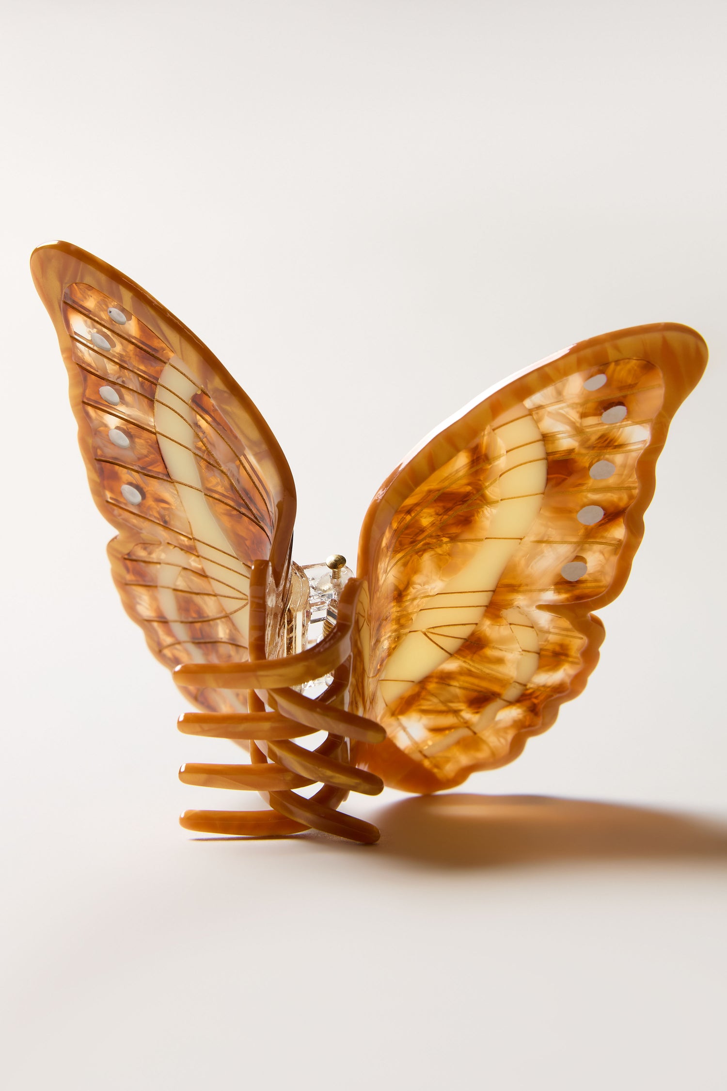 The Hand-Painted Morpho Butterfly Hair Clip is a sculptural accessory with marbled brown and cream wings, shown against a plain, light background.