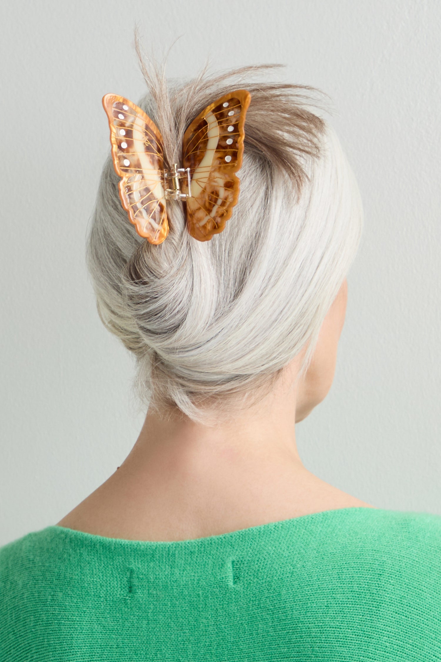 A person with gray hair in a twist, seen from behind wearing a green top, showcases the Hand-Painted Morpho Butterfly Hair Clip as a bold sculptural accessory.