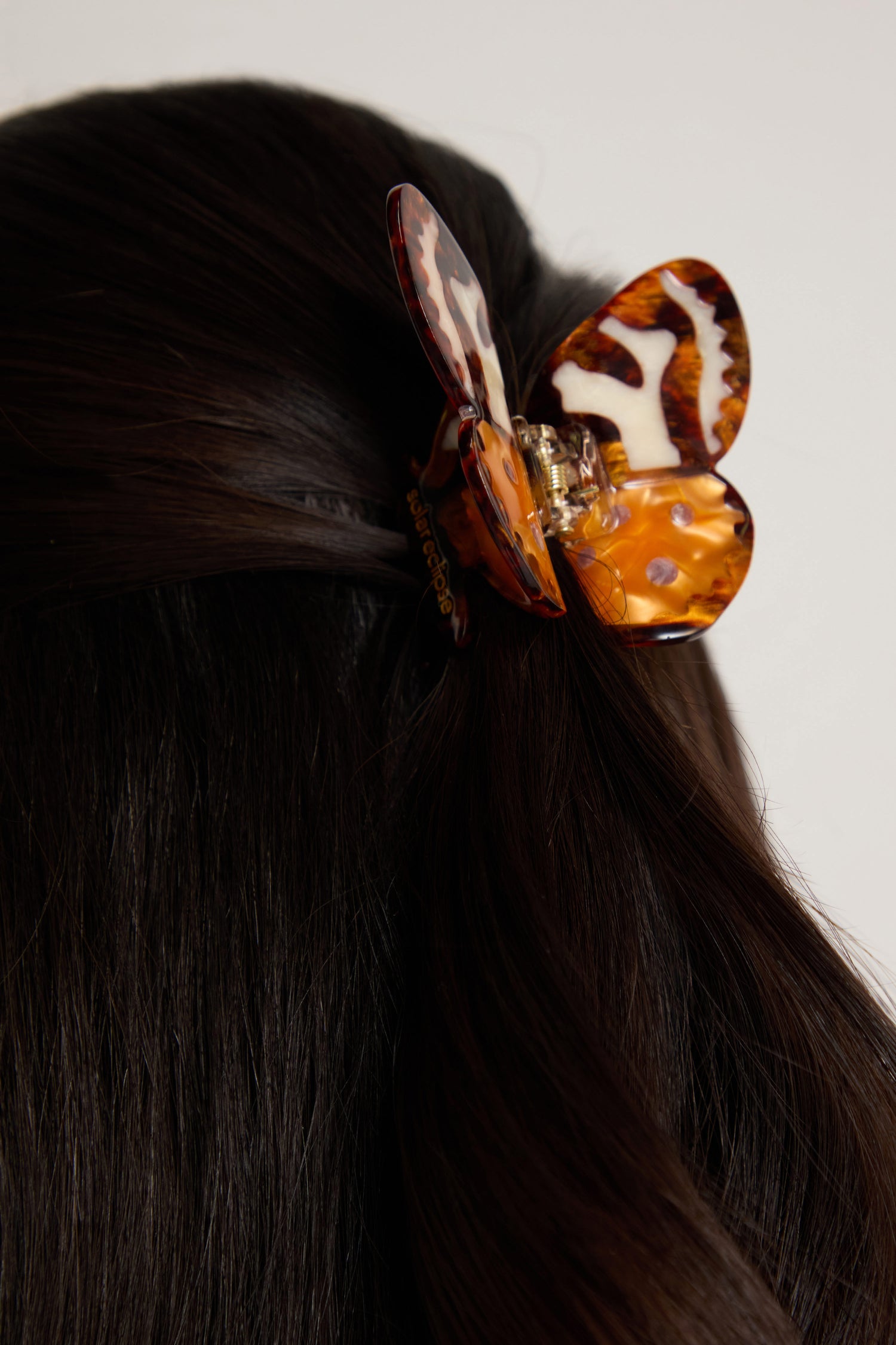 A close-up of dark brown hair styled with the Hand Painted Tiger Moth Hair Clip, featuring a striking eco-friendly tortoiseshell design.