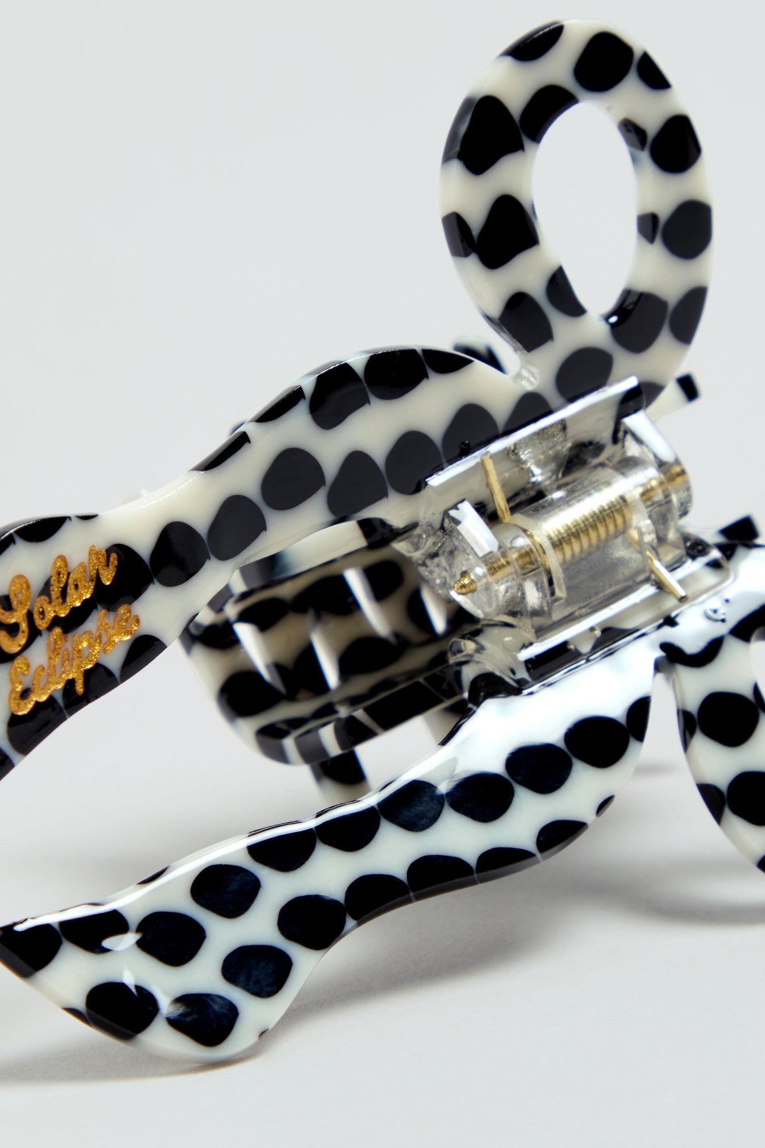 Close-up of a Hand-Painted Coquette Bow Hair Clip made of black and white polka dot cellulose acetate, featuring "Solar Eclipse" written in gold on one side.