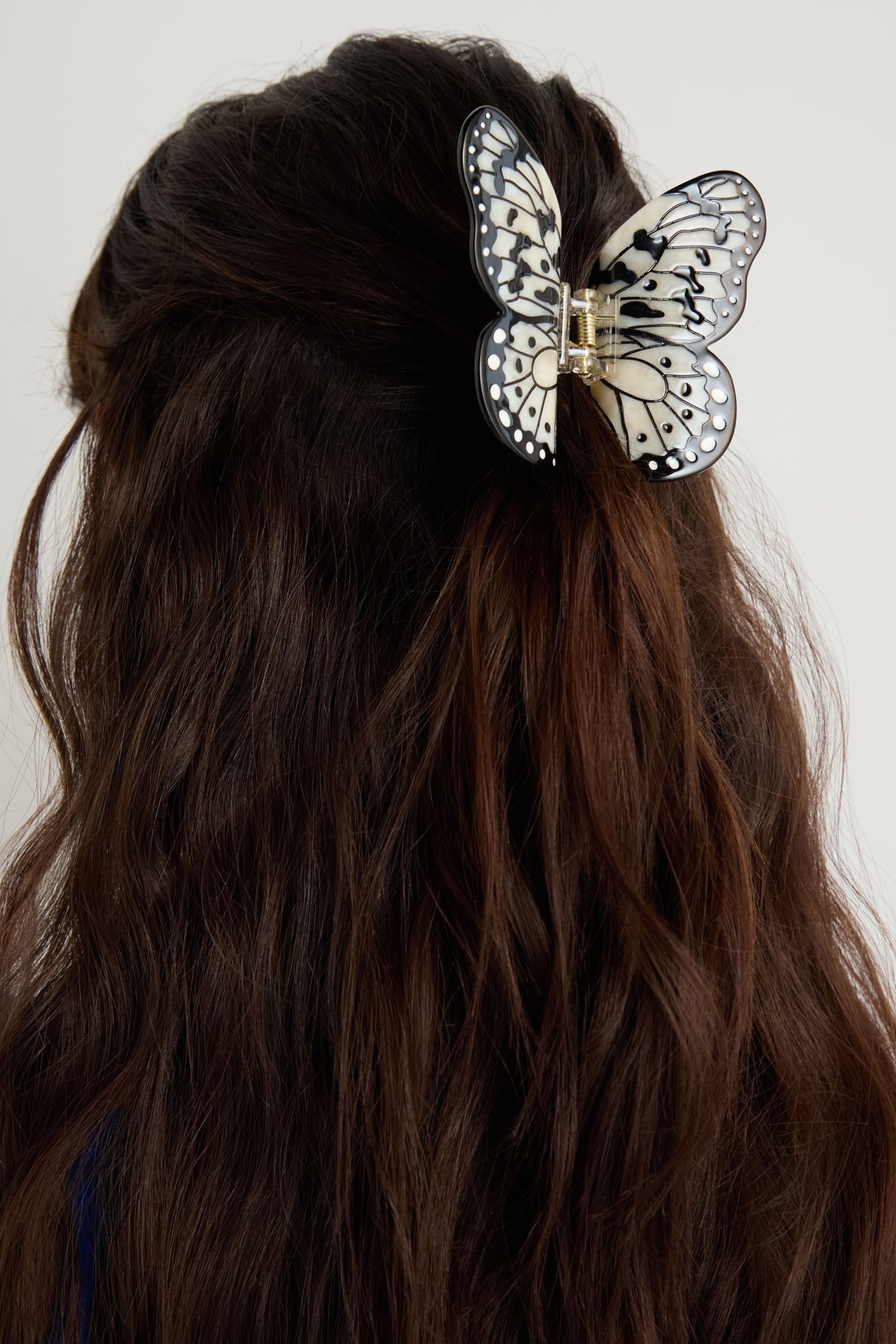 A person with long brown hair wears the Hand-Painted Kite Butterfly Hair Clip, a large eco-friendly black-and-white accessory shaped like a butterfly, at the back of their head.