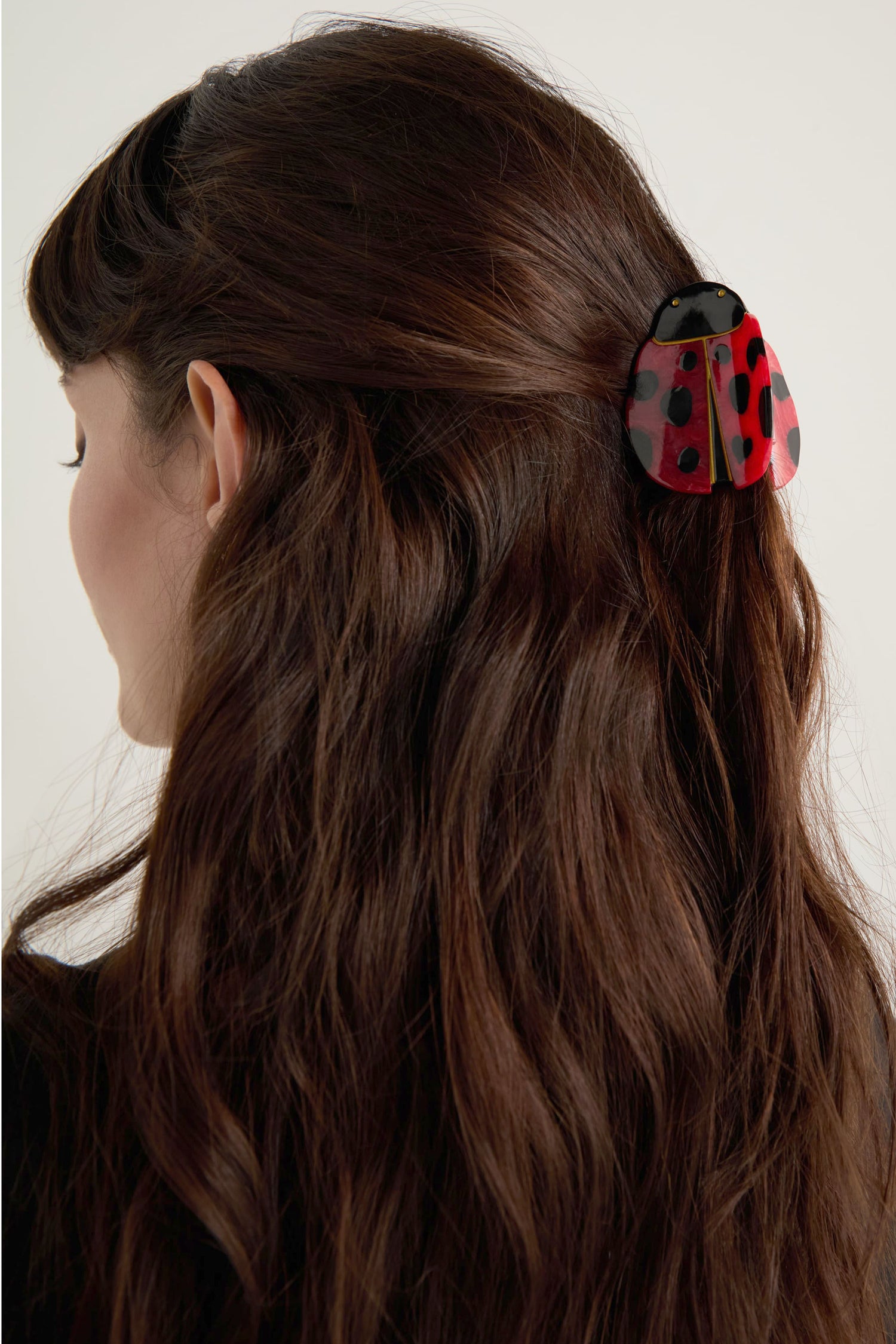 A woman with long brown hair is shown from the back, wearing the Hand-Painted Ladybird Hair Clip in red and black, crafted to be eco-friendly.